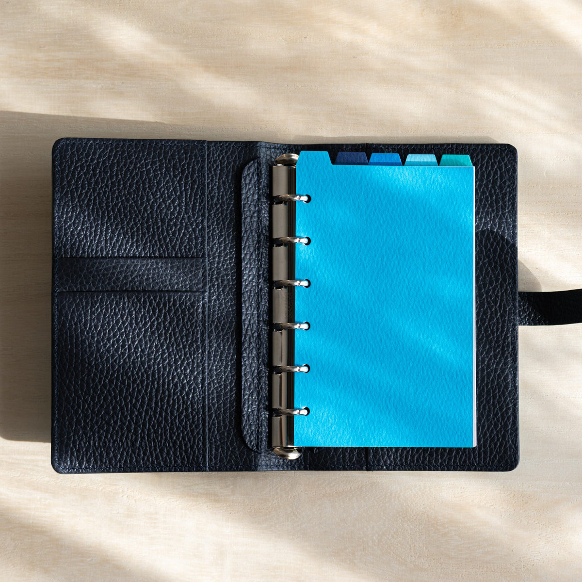 Open Ise Gikakushi planner with navy leather interior and a sky blue tabbed divider on silver rings