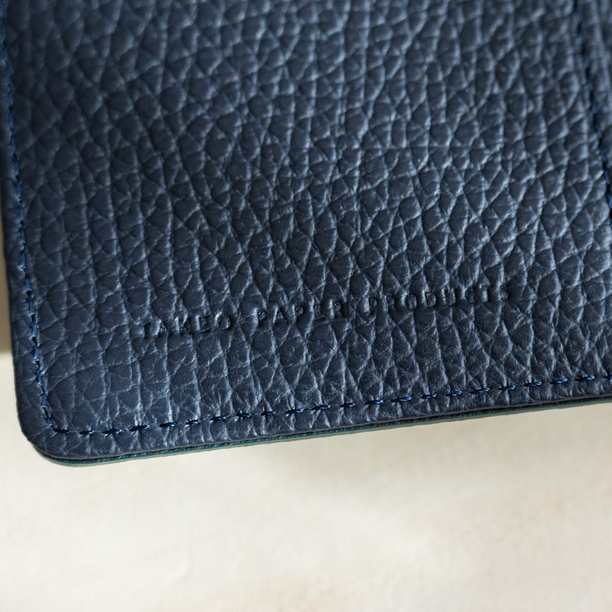 Close-up of the navy pebbled leather interior with debossed TAKEO PAPER PRODUCTS logo and blue stitching