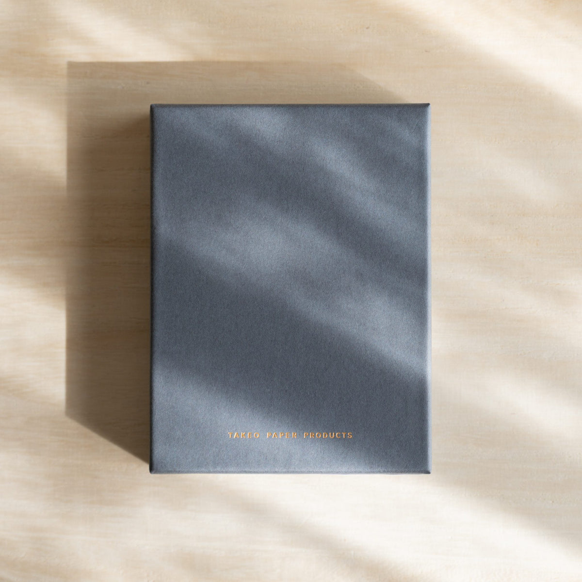 Closed gray TAKEO PAPER PRODUCTS gift box with gold logo along the lower edge