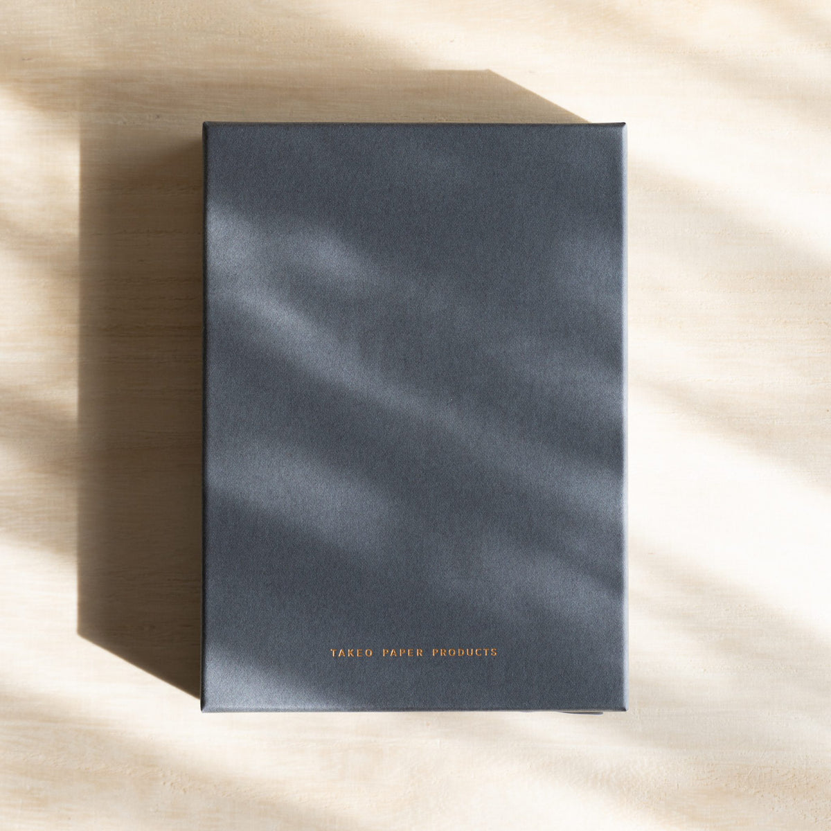 Gray gift box lid with TAKEO PAPER PRODUCTS printed in gold
