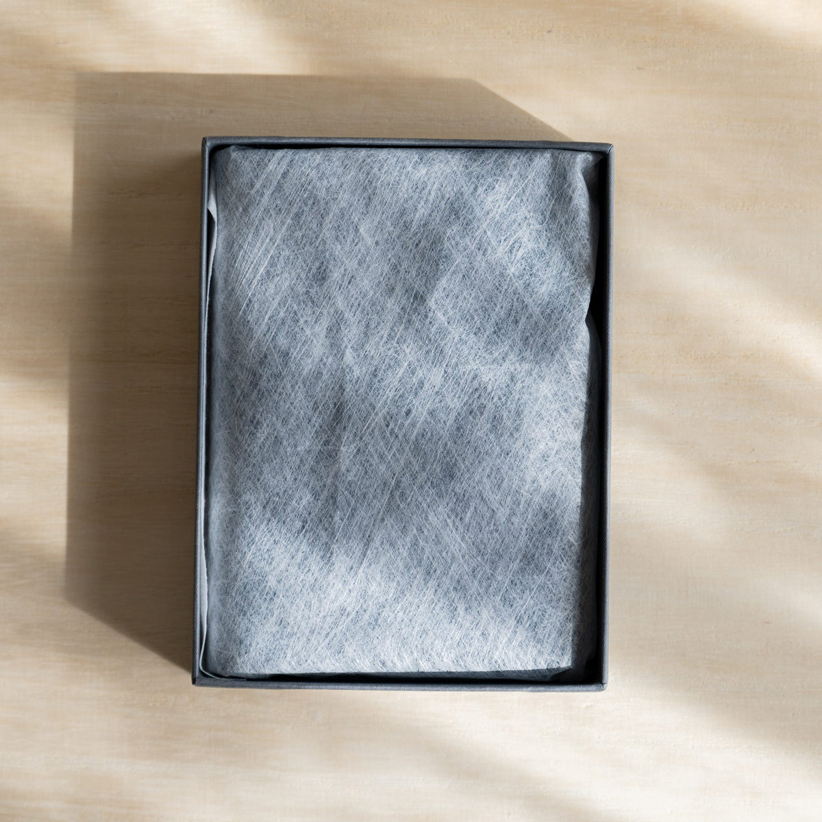 Planner under white nonwoven cloth in an open gray gift box, top view