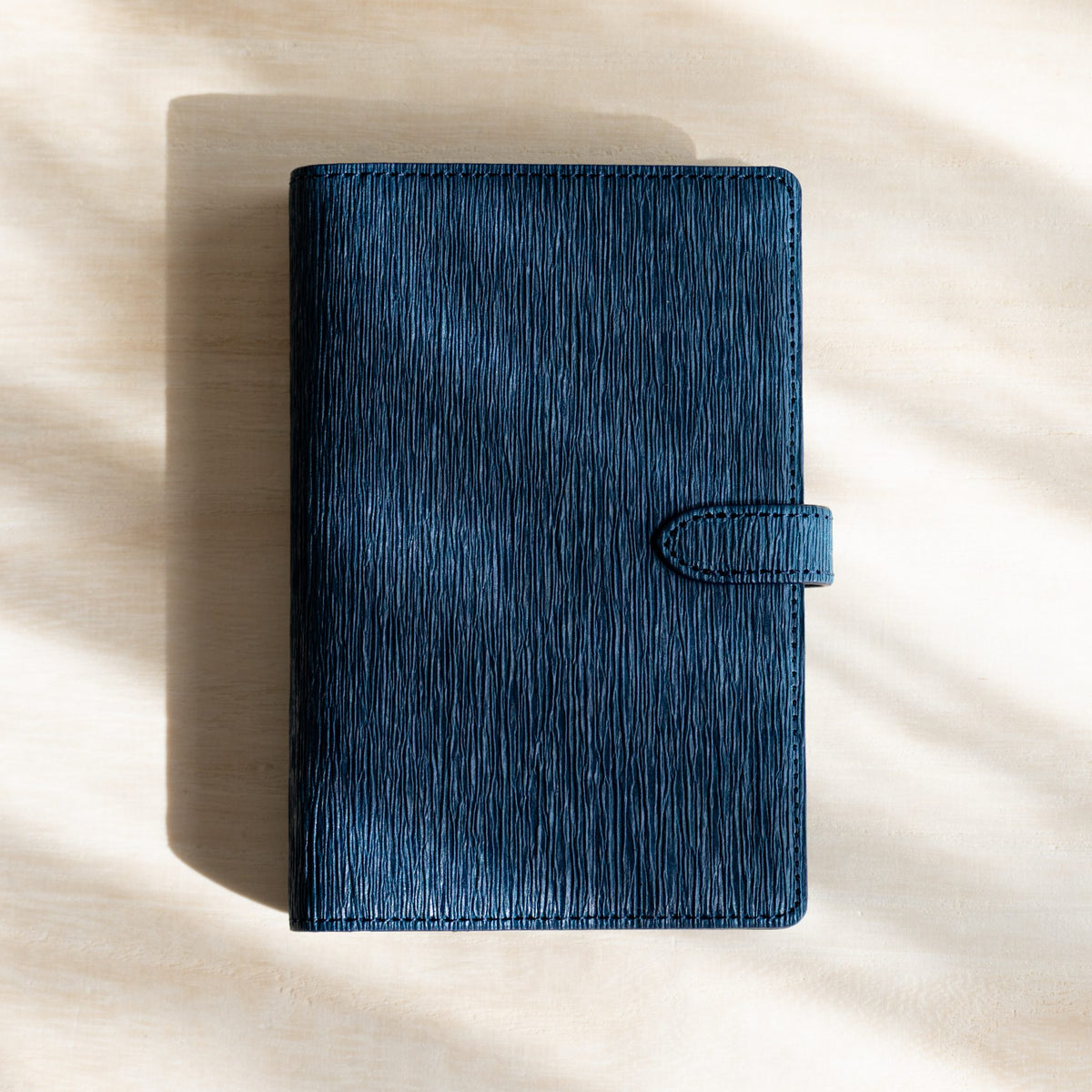 Navy Ise Gikakushi planner lying flat in soft daylight with the strap fastened
