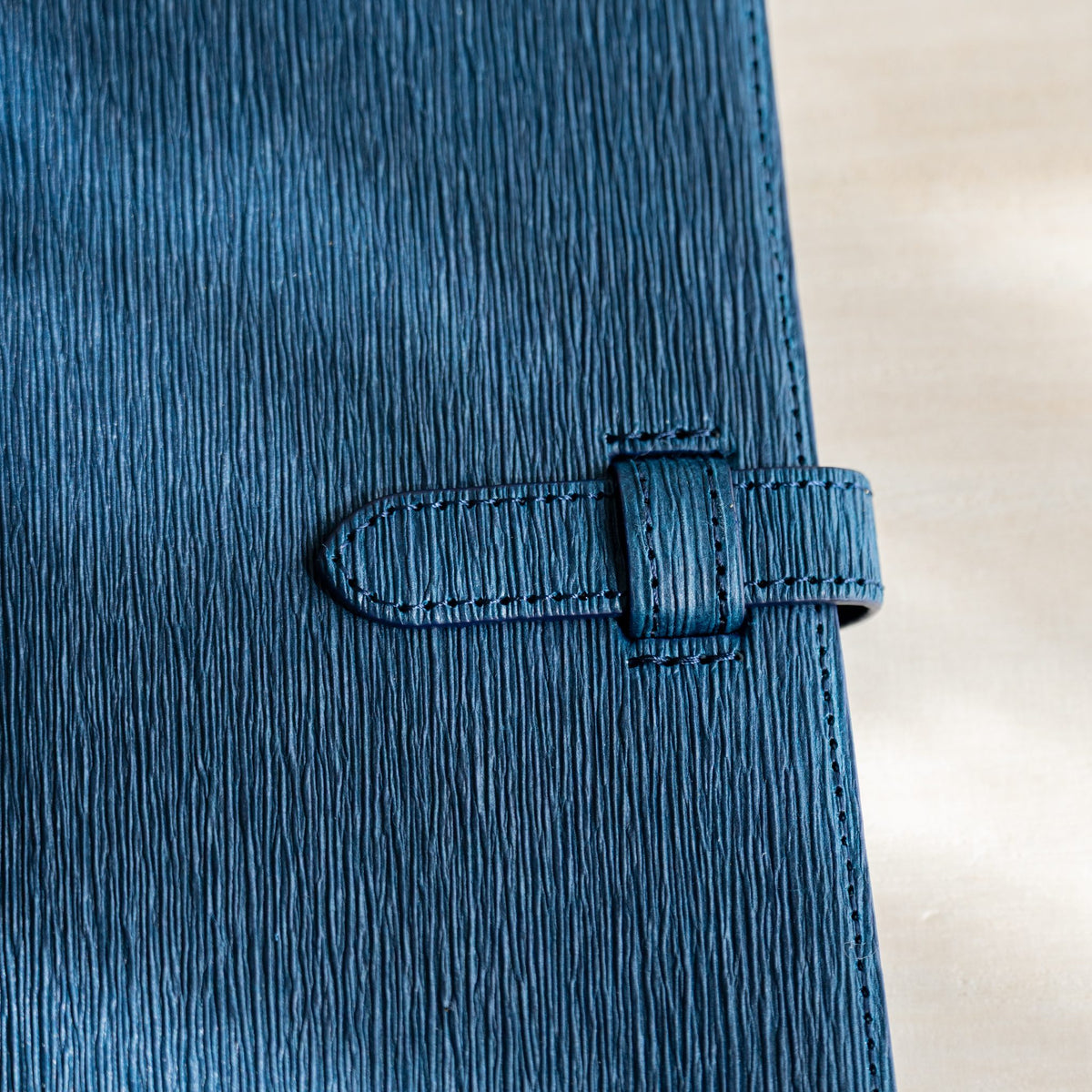 Close-up of navy paper leather creases and the stitched strap with keeper loop