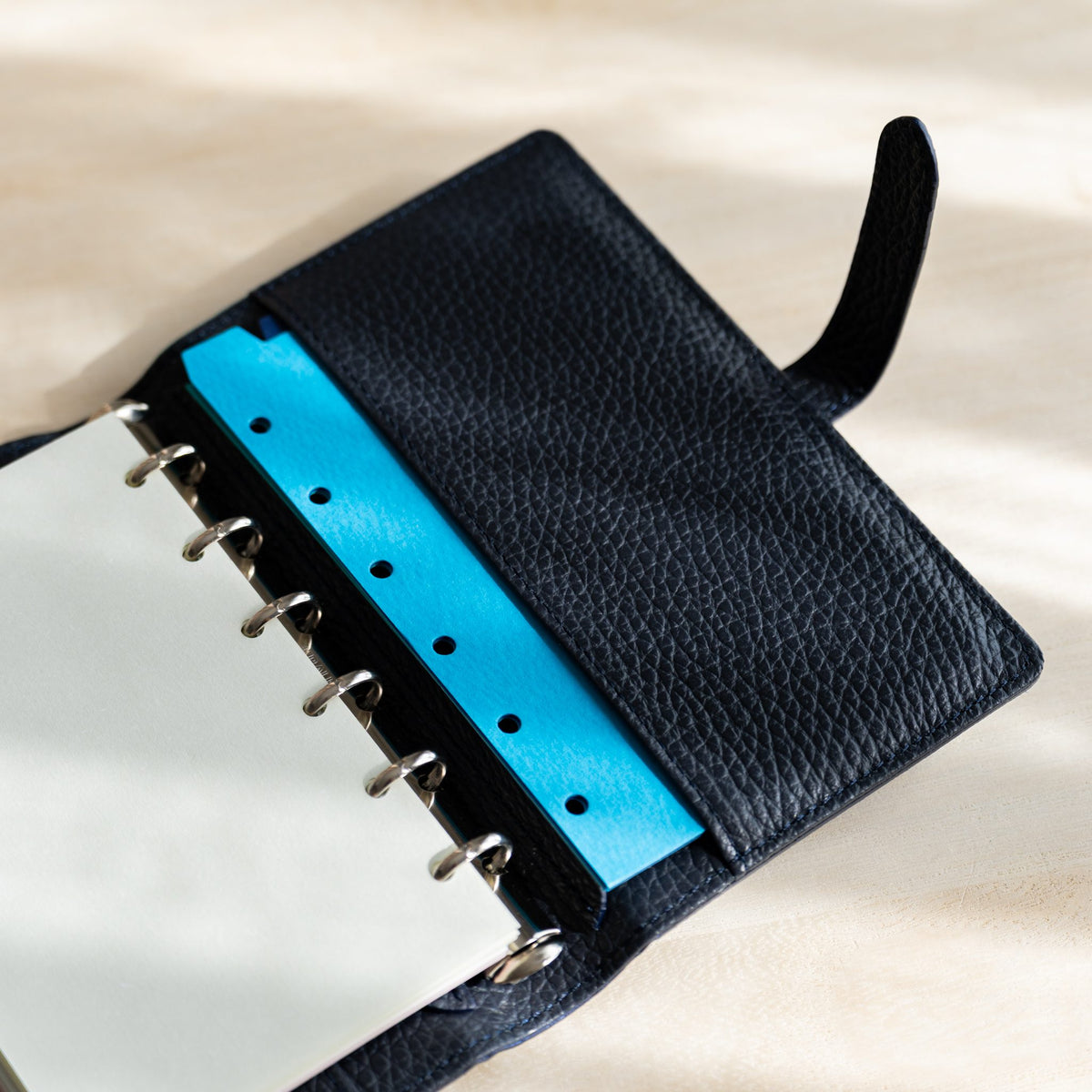 Sky blue hole-punched strip in the navy leather pocket next to cream pages on the rings