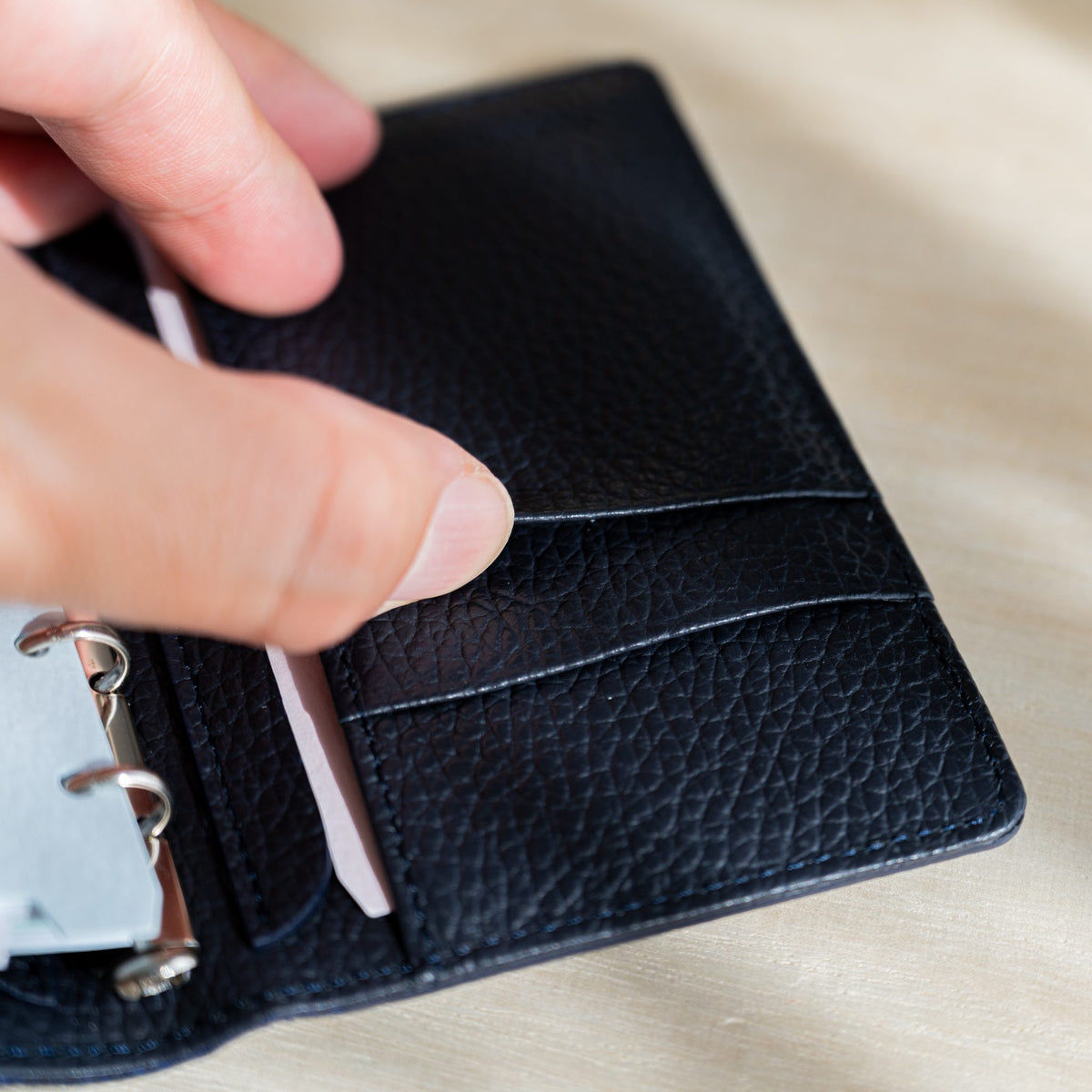 Fingers opening a slip pocket in the navy leather inside cover with a pale pink strip tucked in