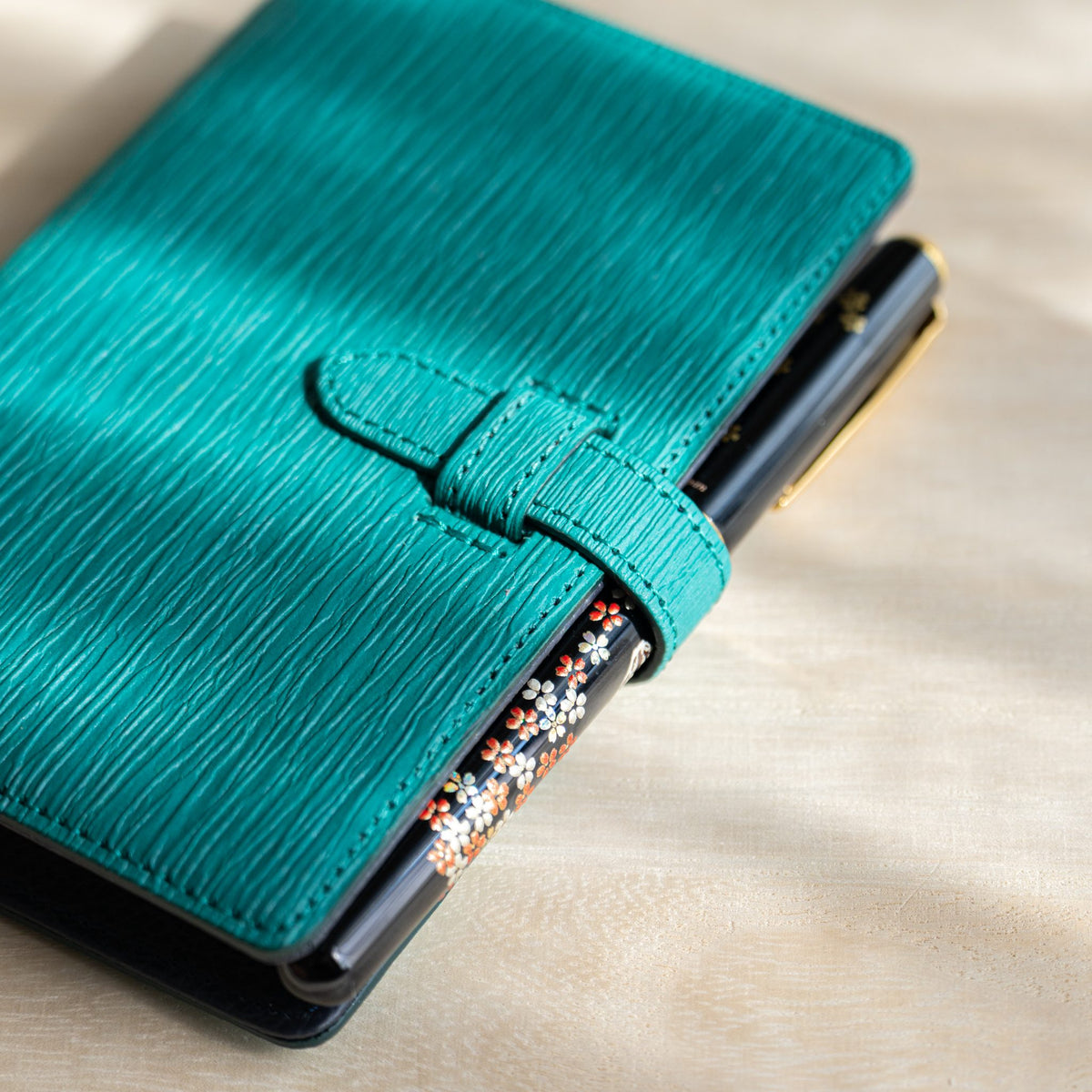 Close-up of the teal strap holding a black fountain pen with floral pattern