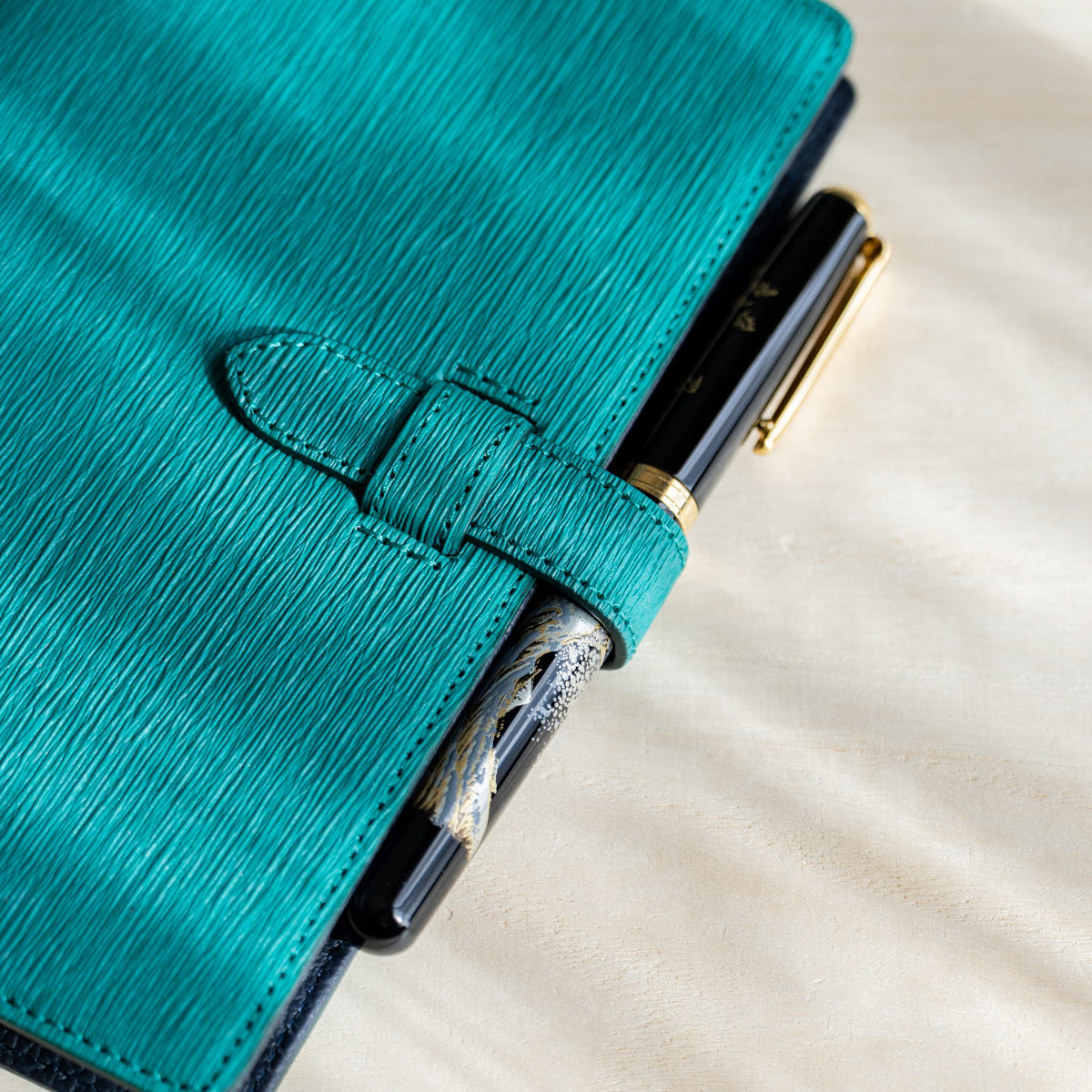 Close-up of the teal paper leather strap holding a black and gold fountain pen at the planner edge