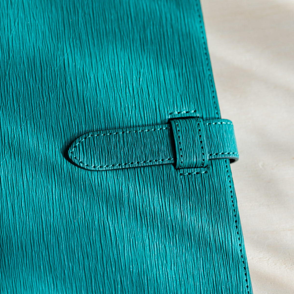 Close-up of the teal Ise Gikakushi paper leather cover showing vertical creases and a stitched strap with loop