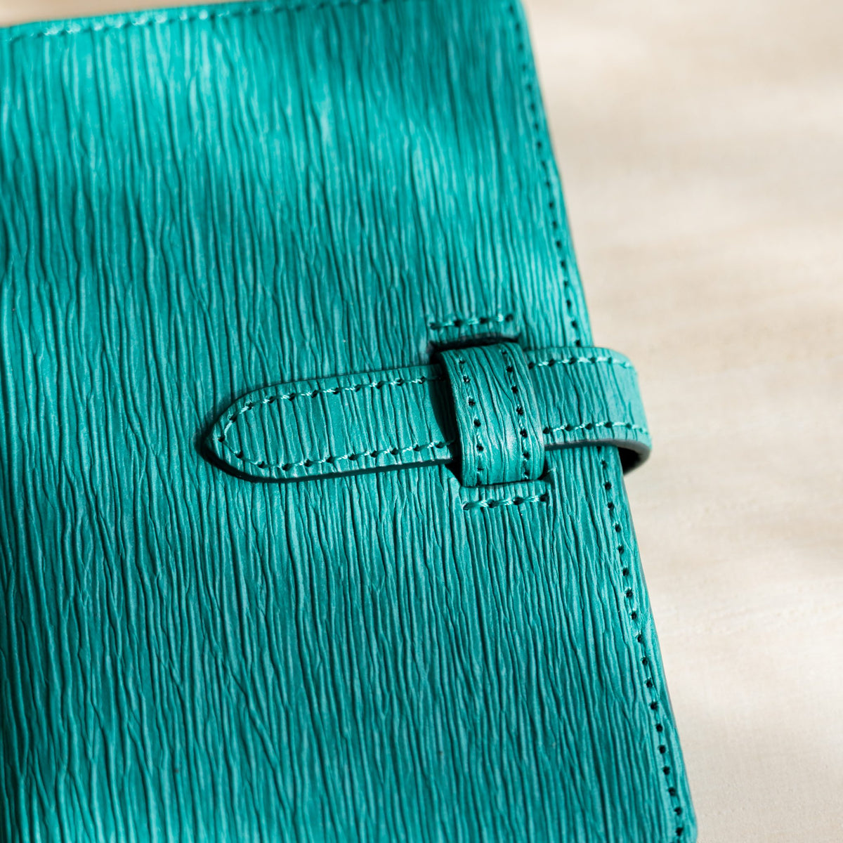 Close-up of the teal paper leather strap and keeper loop with visible stitching and creases
