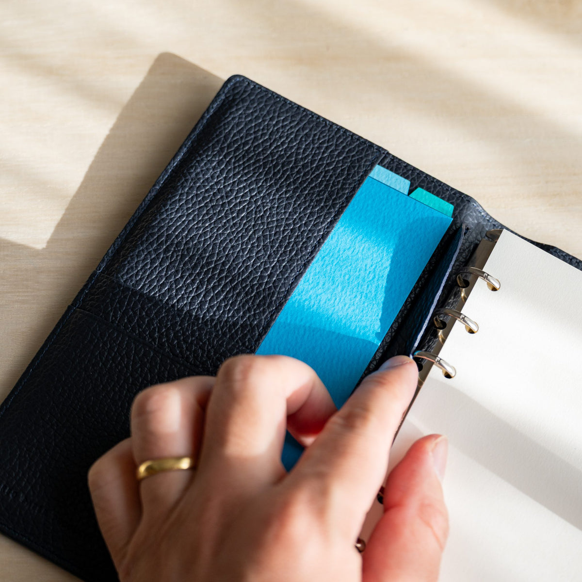 Hand tucking a sky blue sheet into the navy leather pocket of the open Ise Gikakushi planner