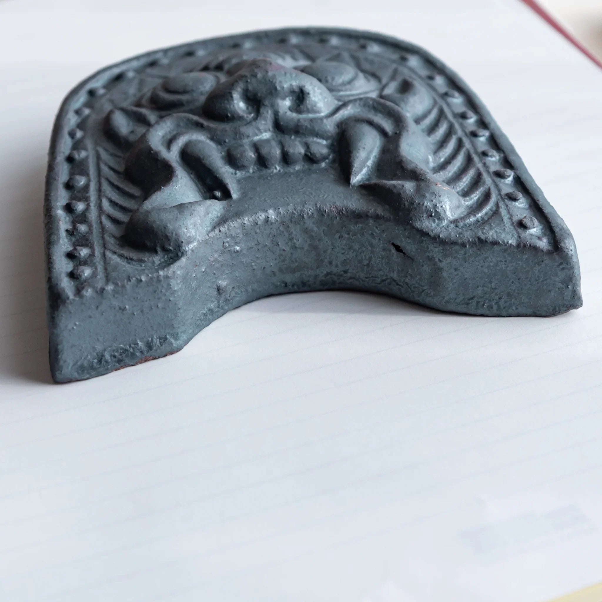 Japanese Paperweight with a oni-gawara tile design placed on top of a piece of paper. Viewed from below.
