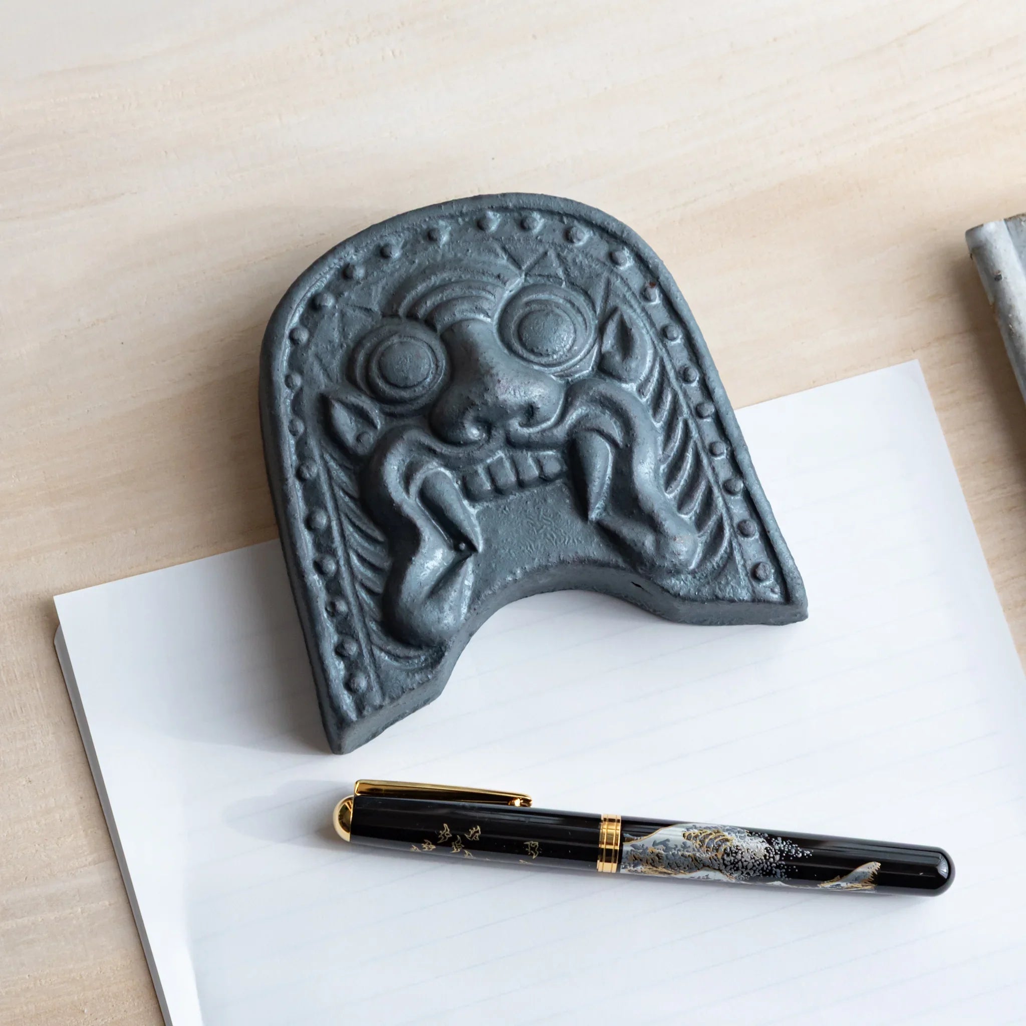 Onigawara-motif Japanese paperweight with a fountain pen placed beside it. A shot of the desk accessory on the paper.