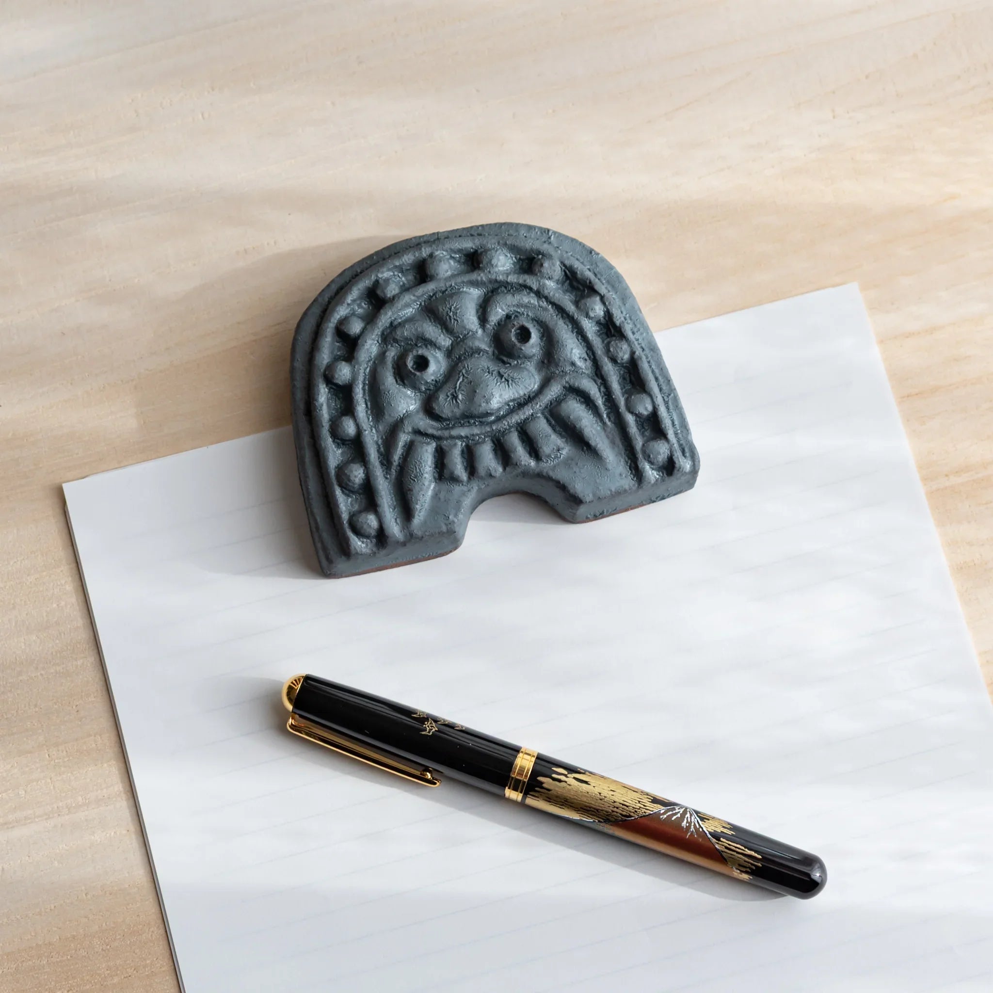 Japanese Paperweight inspired by Oni-gawara tiles resting on paper beside a fountain pen as a refined Japanese Desk Accessory.