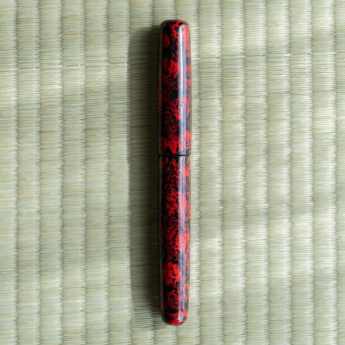 Kagaribi Tsugaru-nuri urushi fountain pen, capped, red and black mottled lacquer, on a tatami mat
