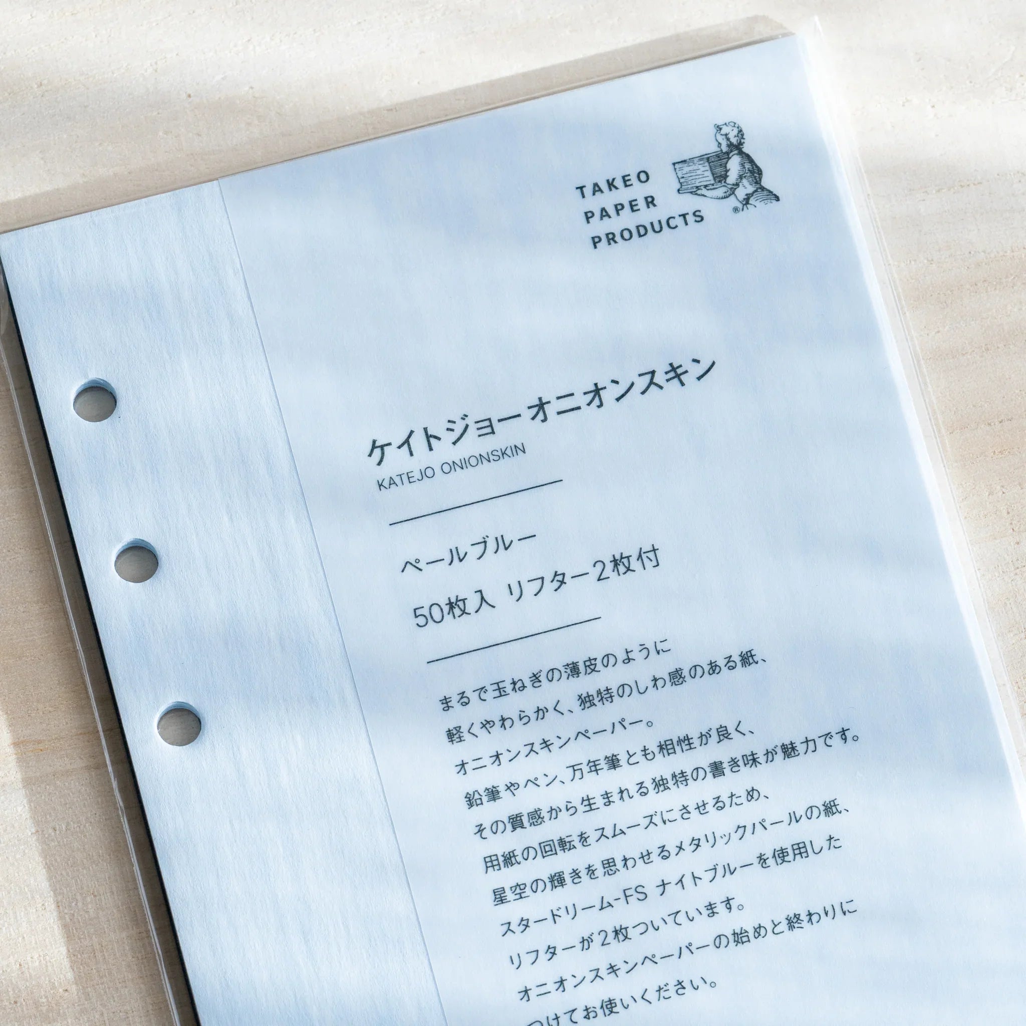 Japanese Stationery pale blue onion skin planner refill with six-hole punches shown in its package on a desk, featuring clear printed details.