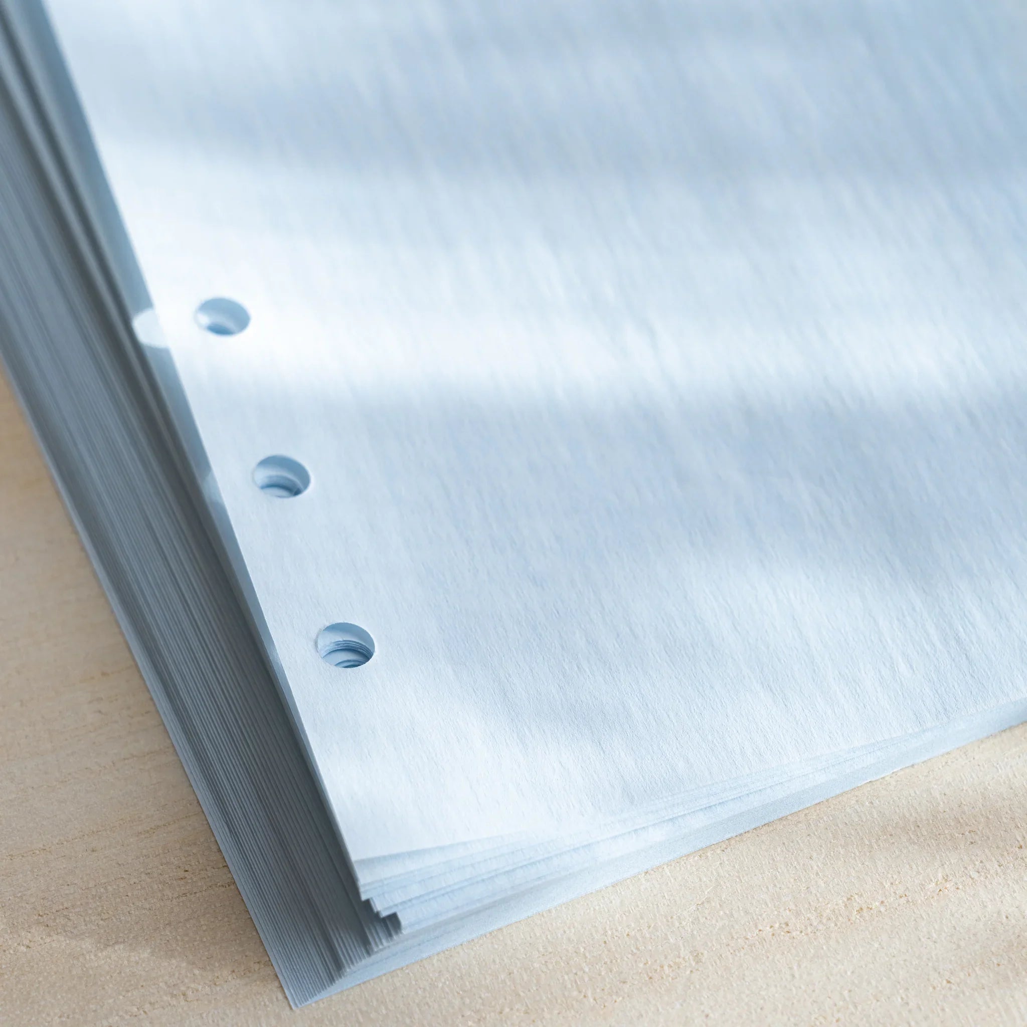 Close-up of pale blue onion skin planner refill sheets showing their thin texture and six-hole punches on a desk.