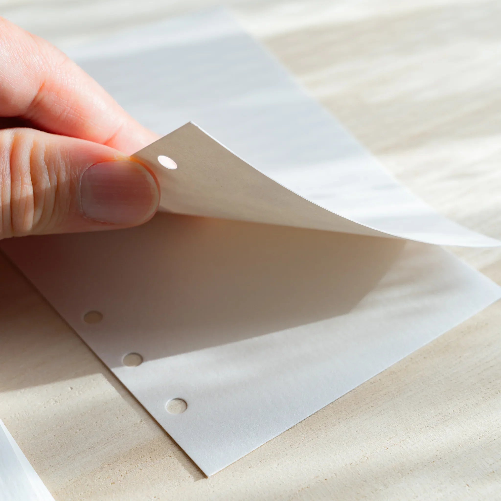 Hand lifting a thin white onion skin planner refill sheet, showing its translucent texture and six-hole punches.