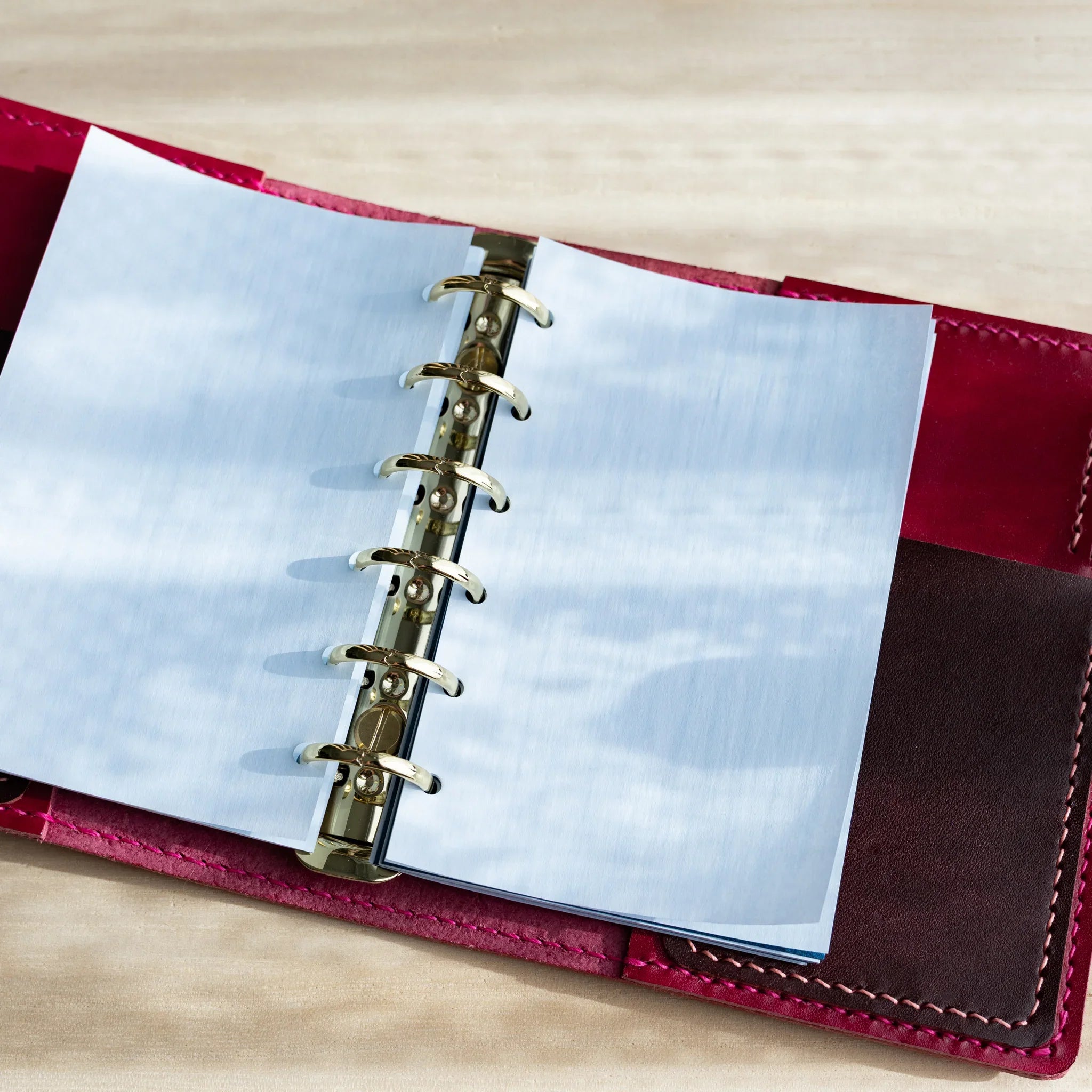 Japanese Stationery pale blue onion skin refill sheets in a mini 6 planner with gold rings and red leather cover on a desk.