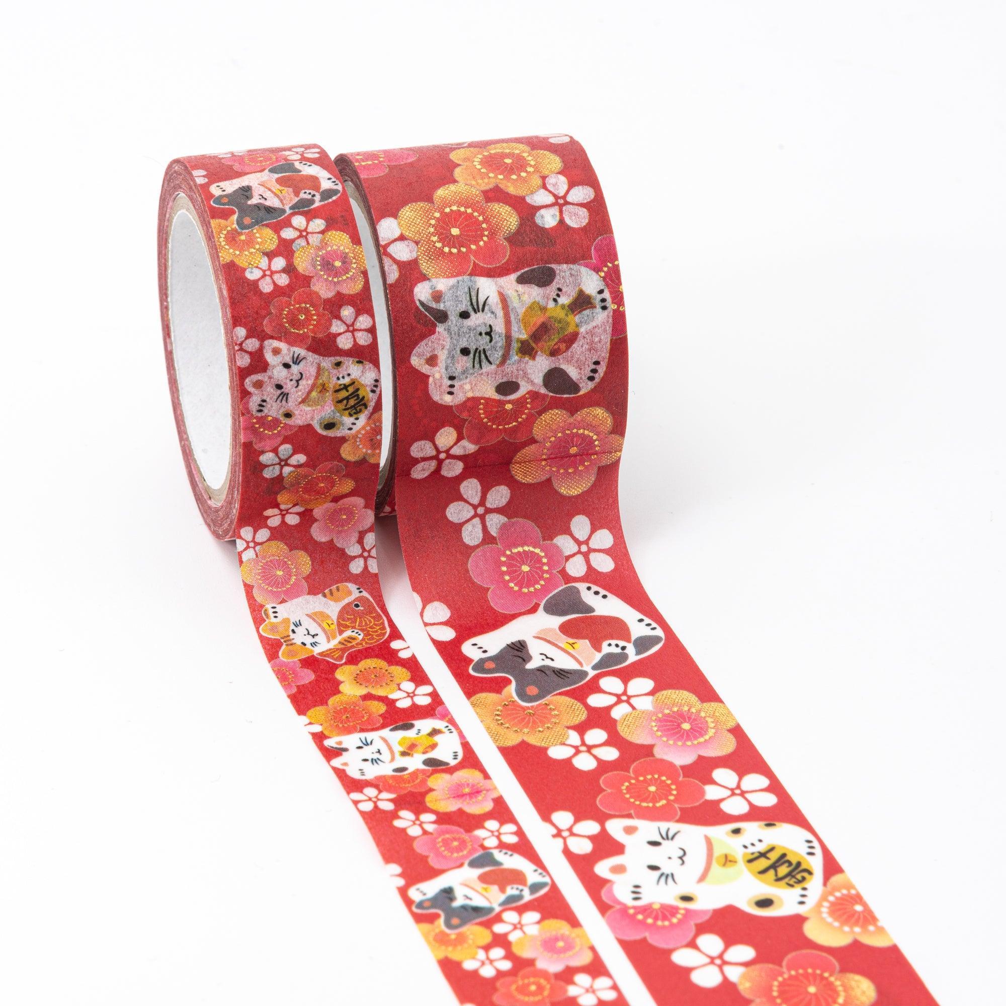 Two rolls of washi tape featuring maneki-neko designs with plum blossoms in red, pink, and gold tones, unrolled to display vibrant details.
