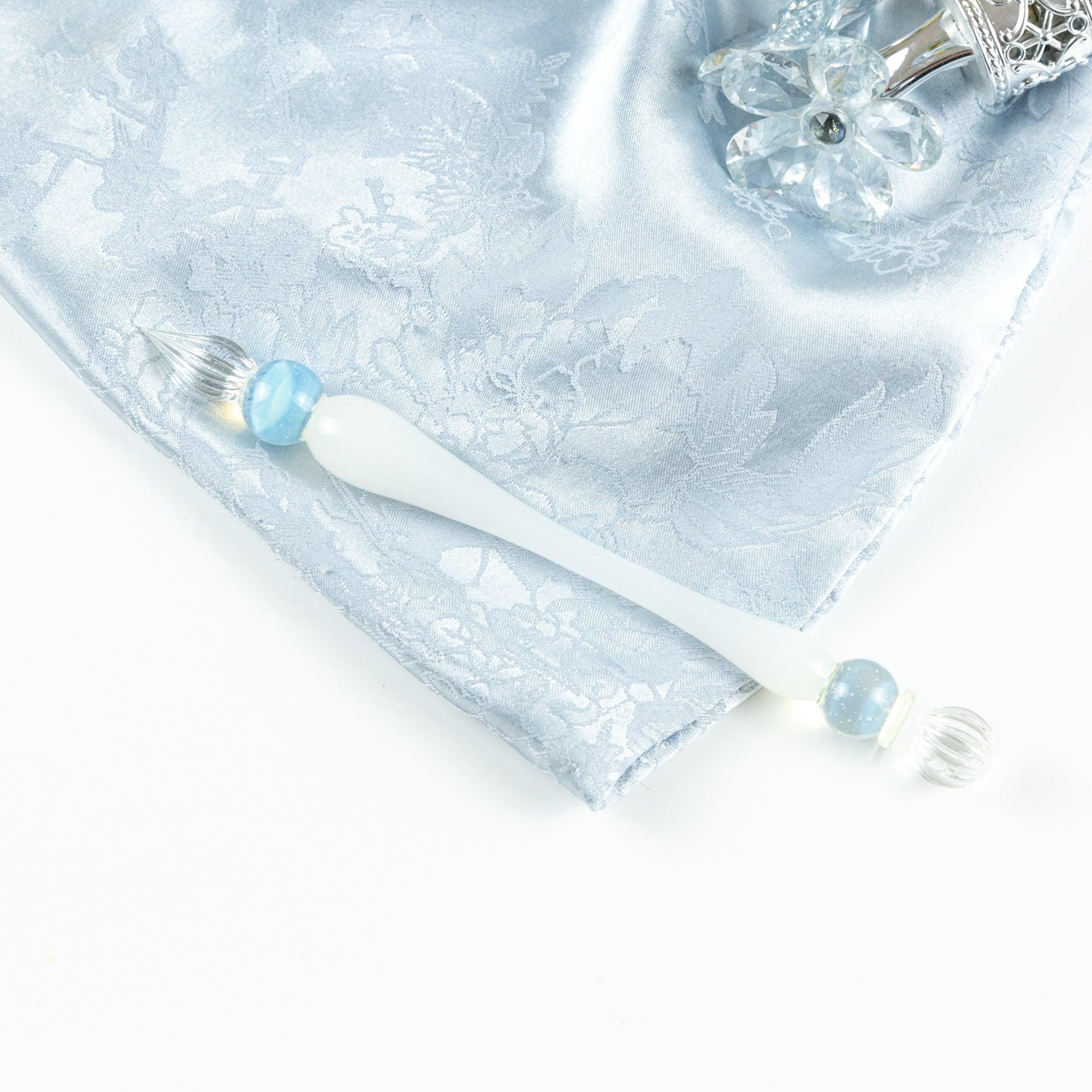Glass pen with white handle and blue sphere, placed on a silver fabric. Great for fans of Japanese stationery and glass pens.