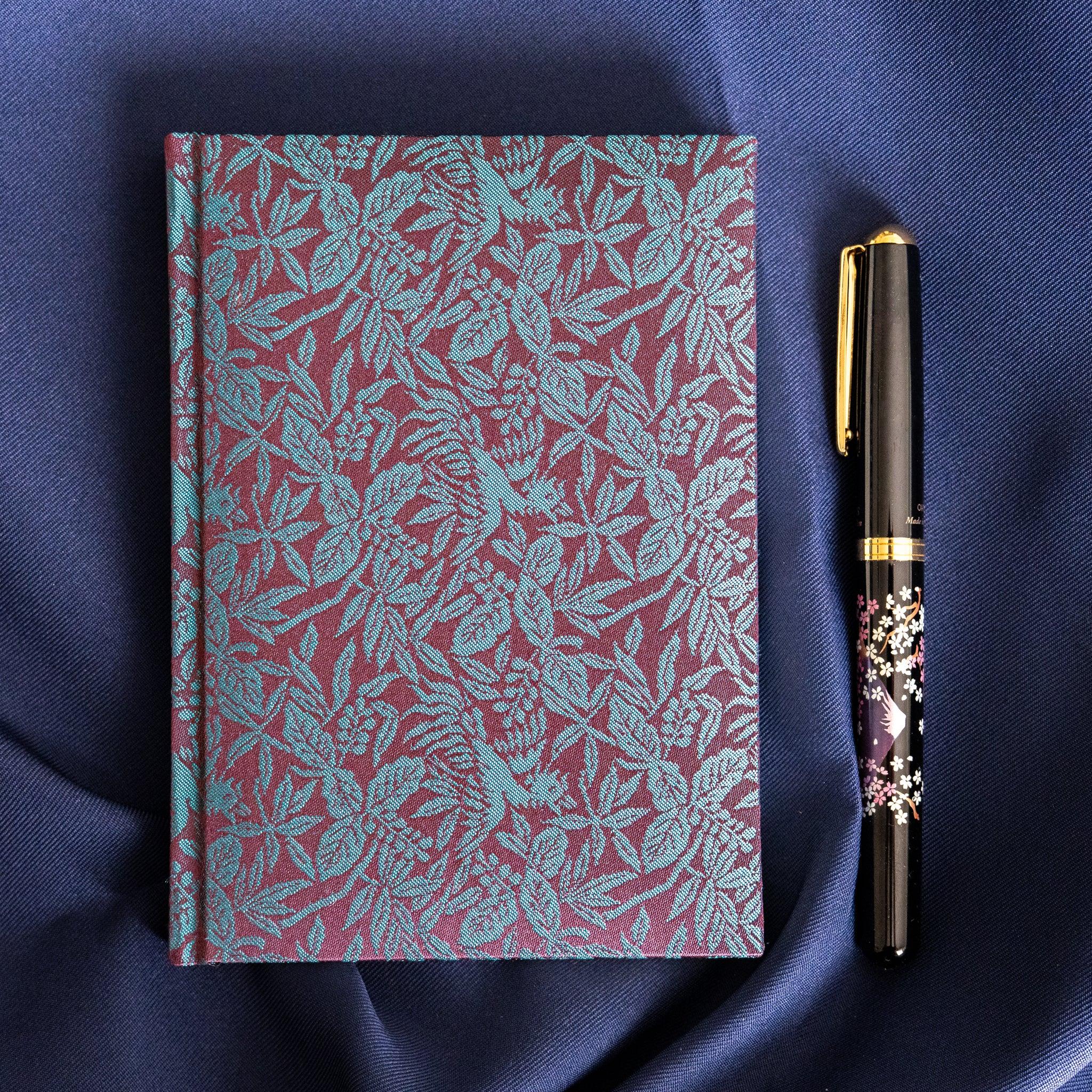 Kiri Take Ho-o Nishijin silk Homeicho notebook alongside decorative maki-e fountain pen on navy fabric
