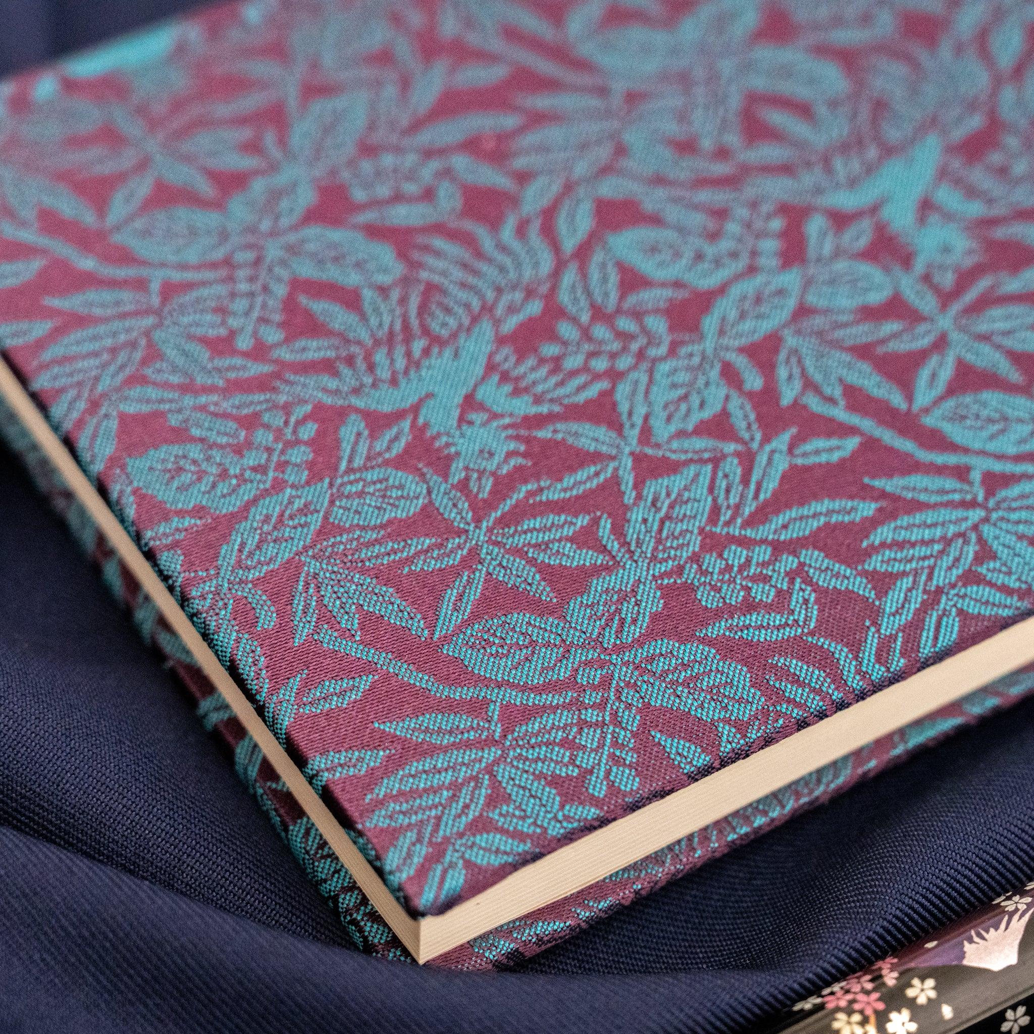 Kiri Take Ho-o Nishijin silk notebook corner view showing page edges and teal woven silk cover with pen on navy fabric
