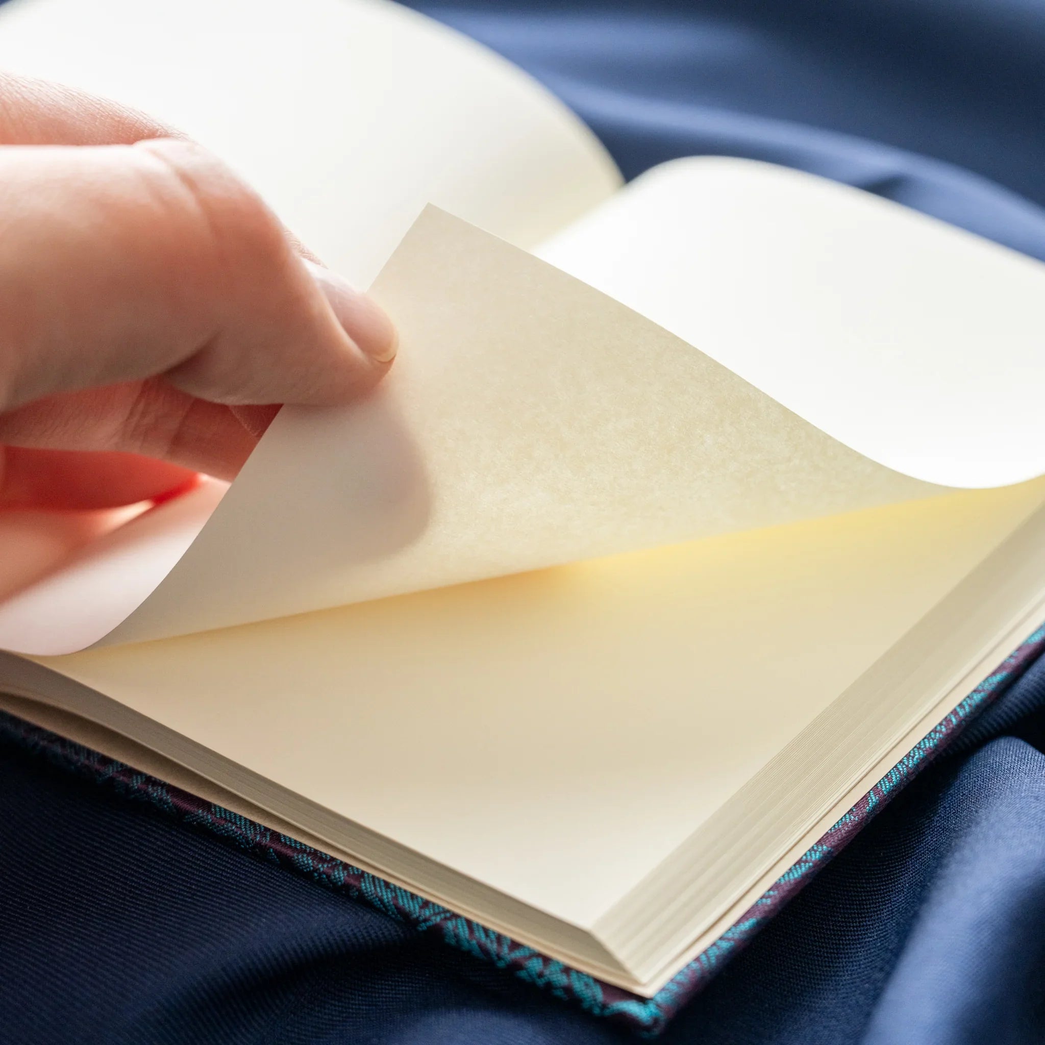 Hand turning pages of Kiri Take Ho-o Nishijin silk notebook revealing cream Kohaku paper with teal cover base