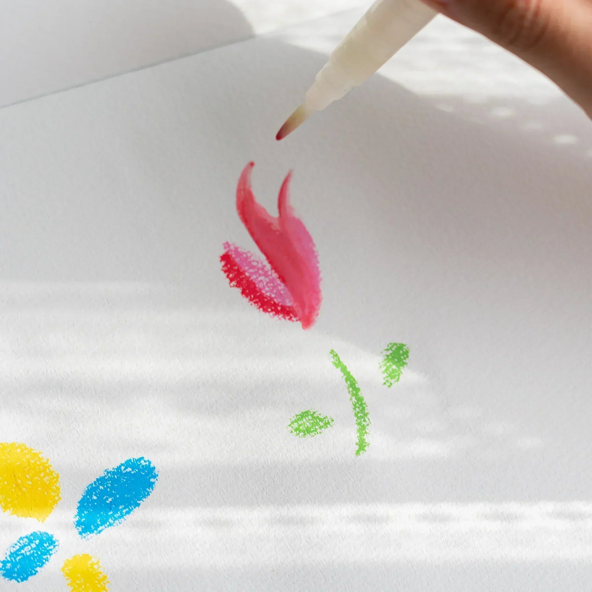 Water brush pen blending red and pink kitpas watercolor crayon marks on white paper, showing soft color mixing effects.