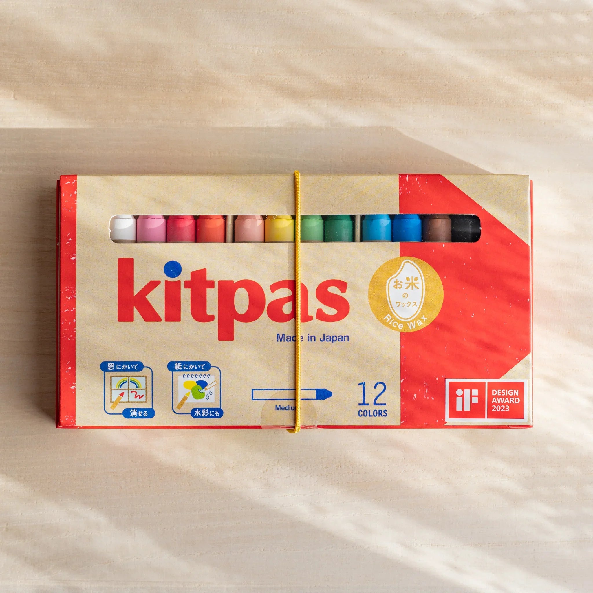 Kitpas watercolor crayons set of 12 in a beige box with red label, wrapped by elastic band, on neutral background.