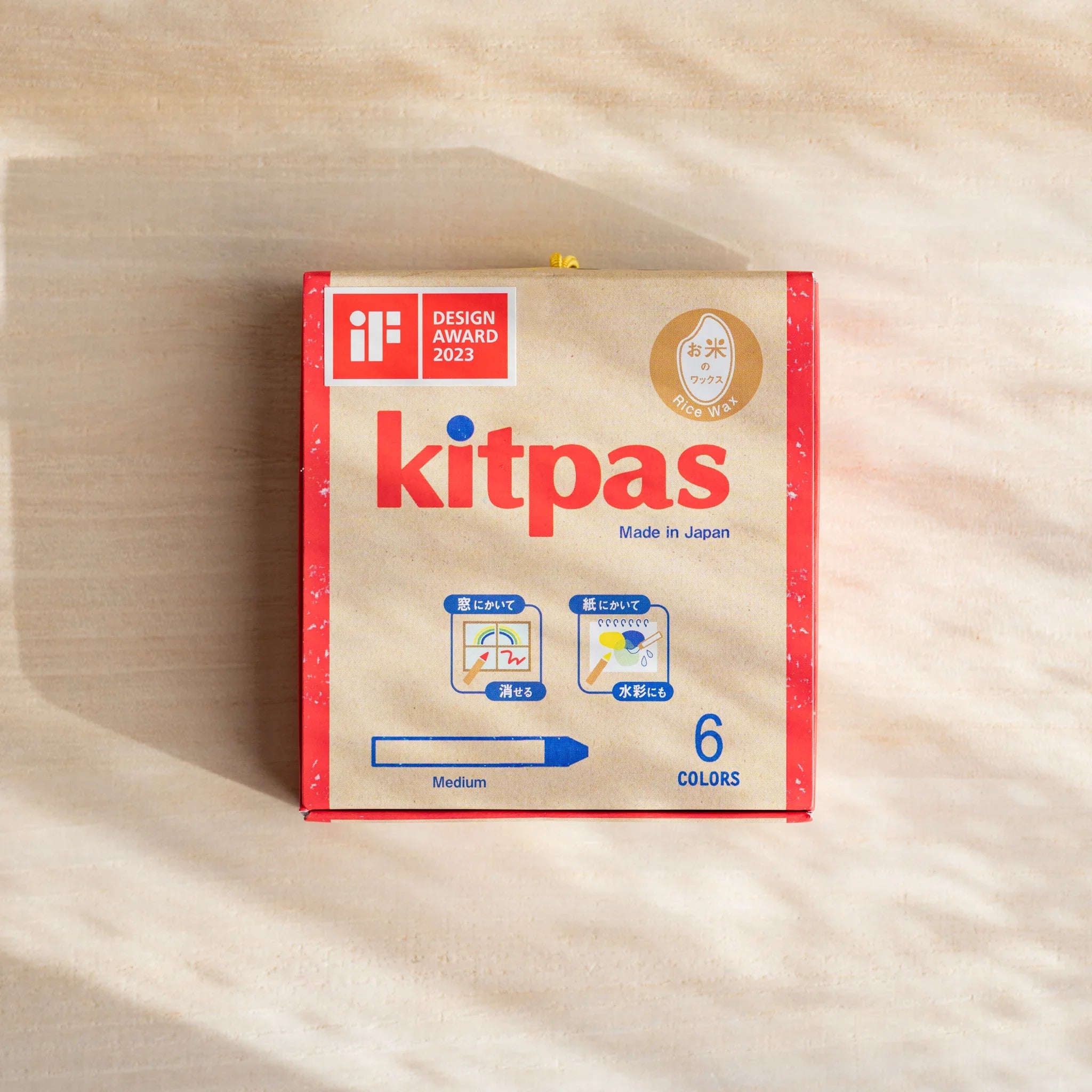 Front view of kitpas 6-color non-toxic rice wax watercolor crayons in beige packaging on a cream cloth background.