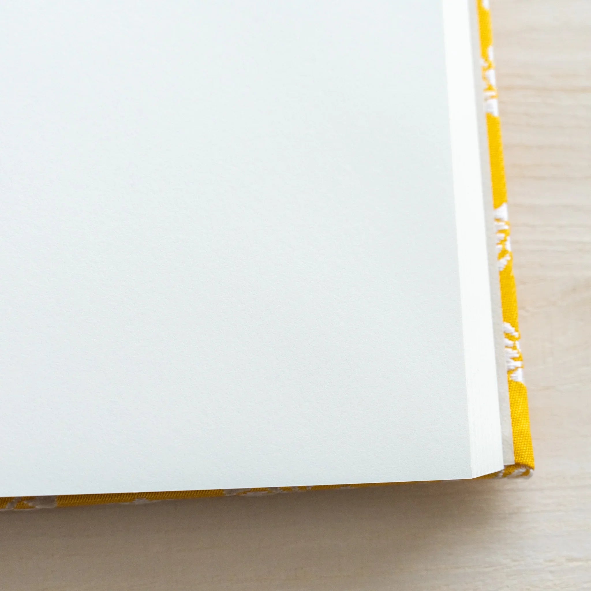 Close-up corner of Ko Aoi Nishijin Homeicho notebook showing clean white pages and golden cover edge on wood surface