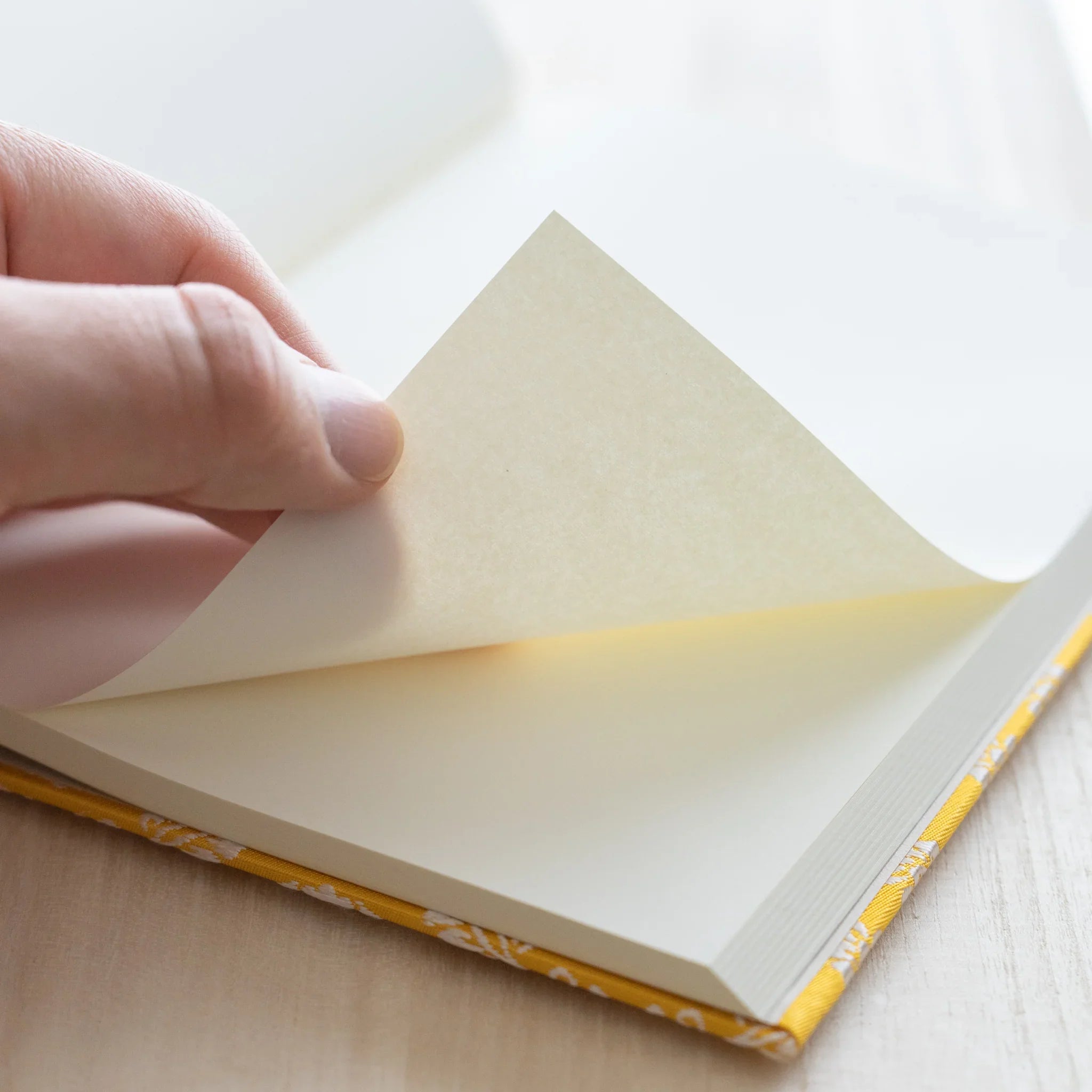 Hand turning page of Ko Aoi Nishijin silk Homeicho notebook showing smooth Rough Cream paper texture and golden cover