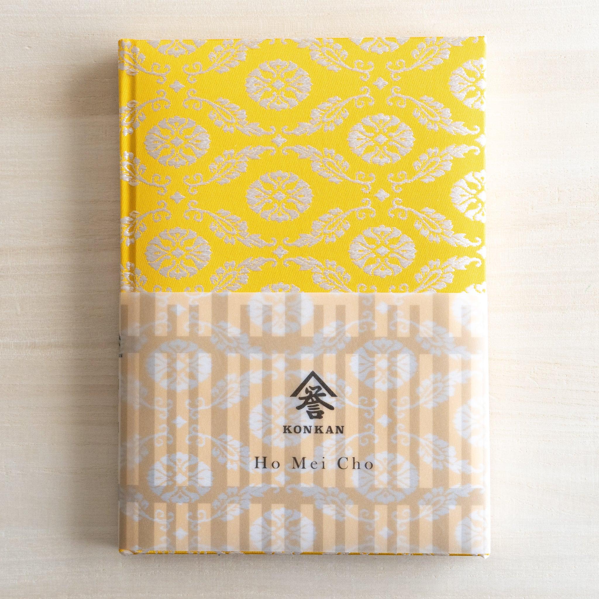 Ko Aoi Nishijin silk Homeicho notebook with KONKAN Ho Mei Cho paper band on cream background, golden floral cover