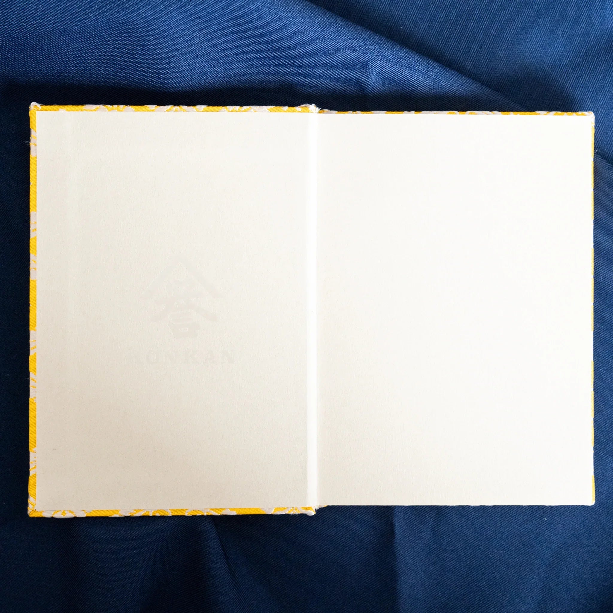 Ko Aoi Nishijin silk Homeicho notebook opened flat overhead showing blank white pages with golden cover border on navy fabric