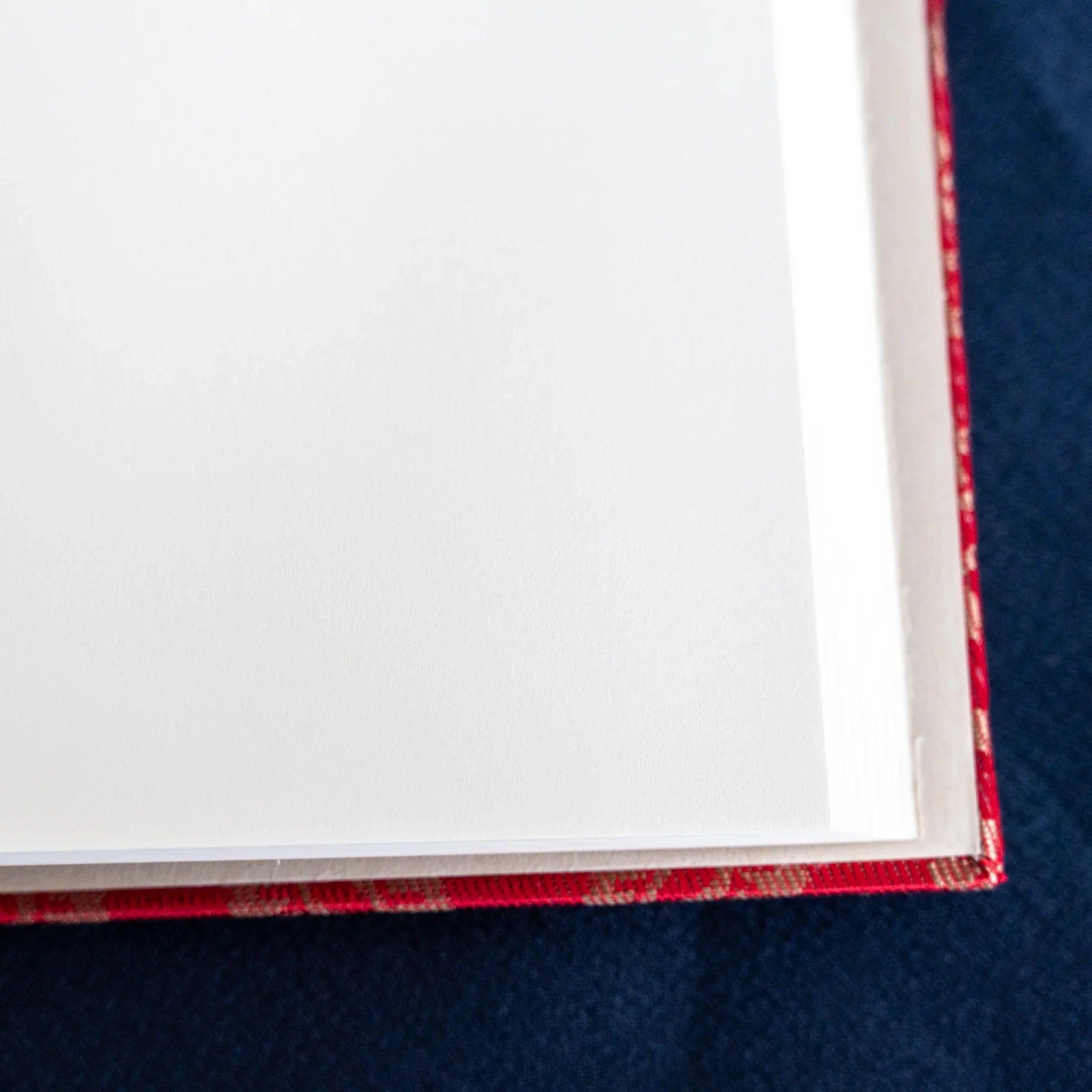 Close-up corner of Ko Aoi Nishijin Homeicho notebook showing clean white pages and vermilion cover edge on blue fabric