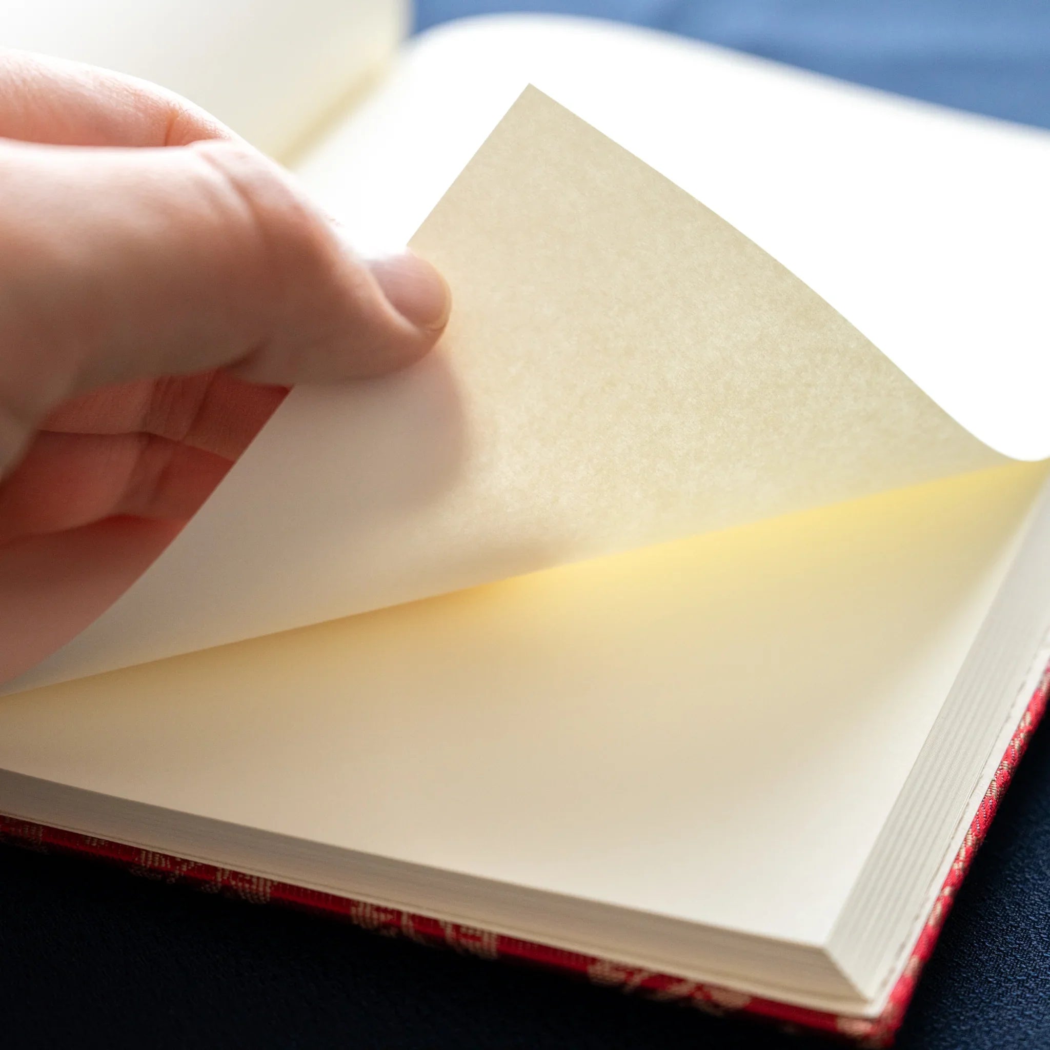Hand turning page of Ko Aoi Nishijin silk Homeicho notebook showing smooth cream Rough Cream paper texture