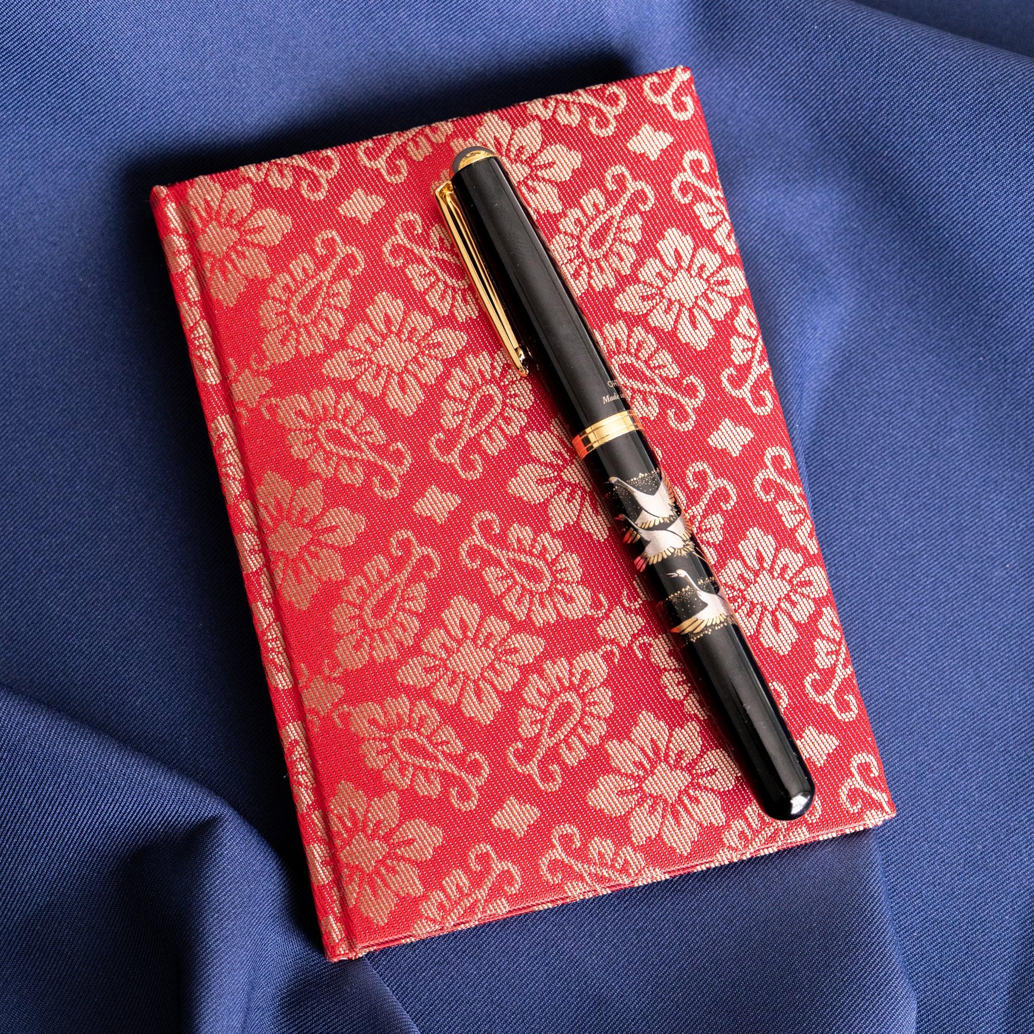 Ko Aoi Nishijin silk Homeicho notebook on blue fabric with black gold fountain pen placed diagonally across the cover