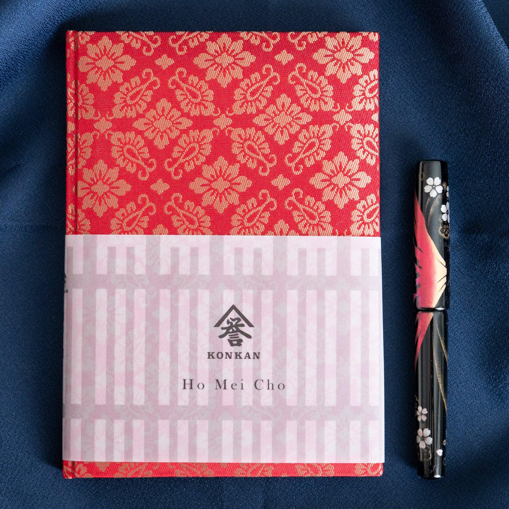 Ko Aoi Nishijin silk Homeicho notebook with paper band reading KONKAN Ho Mei Cho beside decorative fountain pen on blue