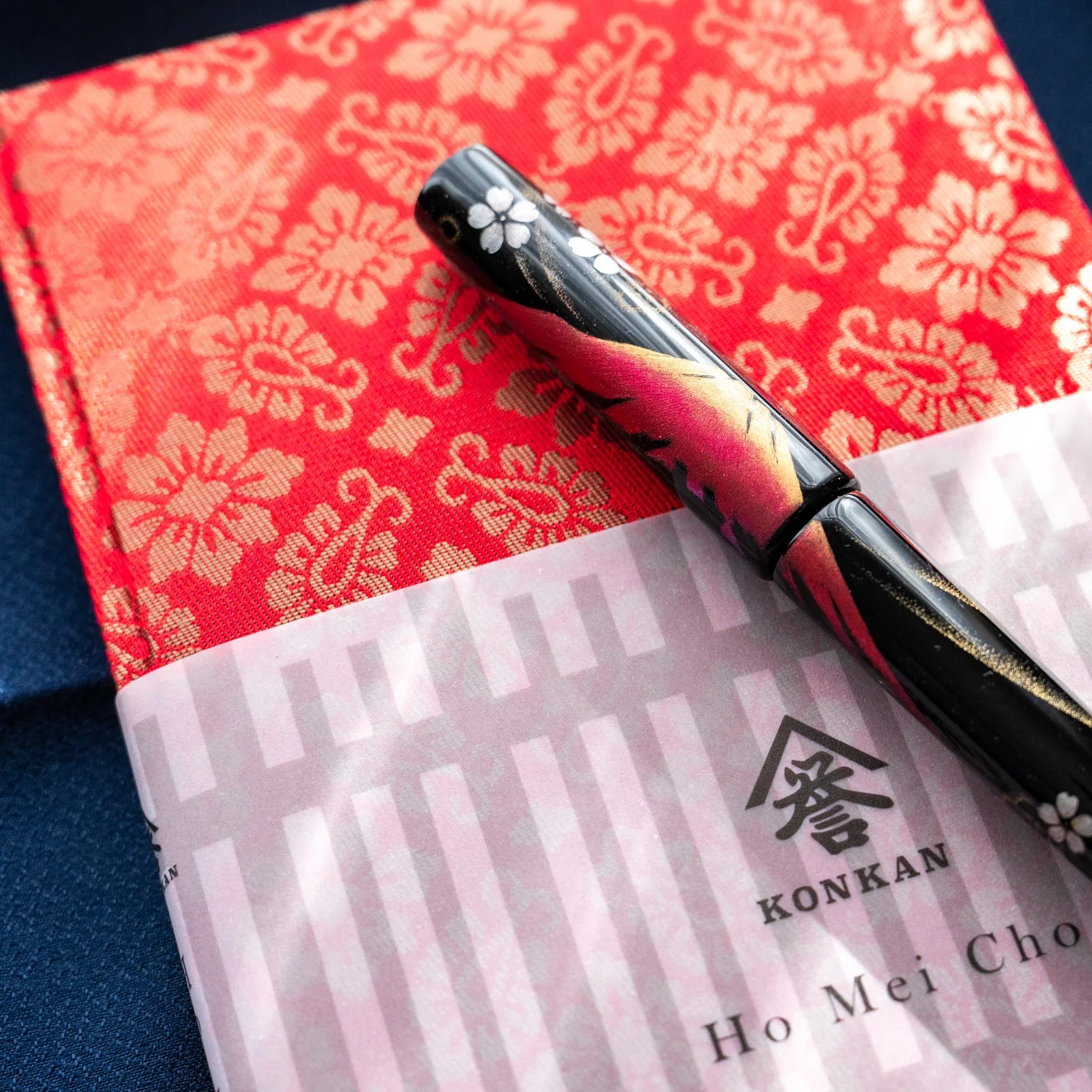 Ko Aoi Nishijin silk notebook corner with vermilion pattern and pen resting on KONKAN Ho Mei Cho paper band