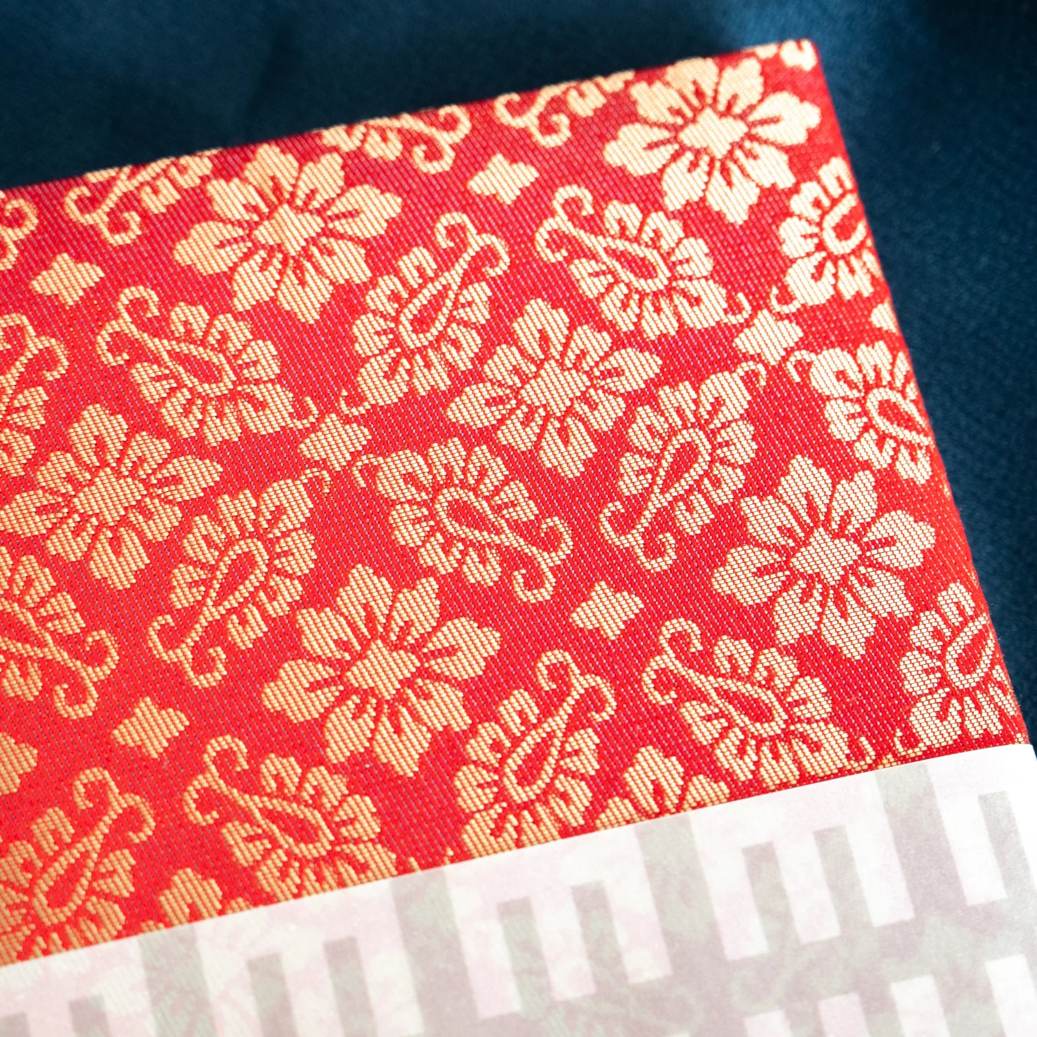 Close-up angled view of Ko Aoi Nishijin silk cover showing white hollyhock floral weave pattern on vermilion fabric