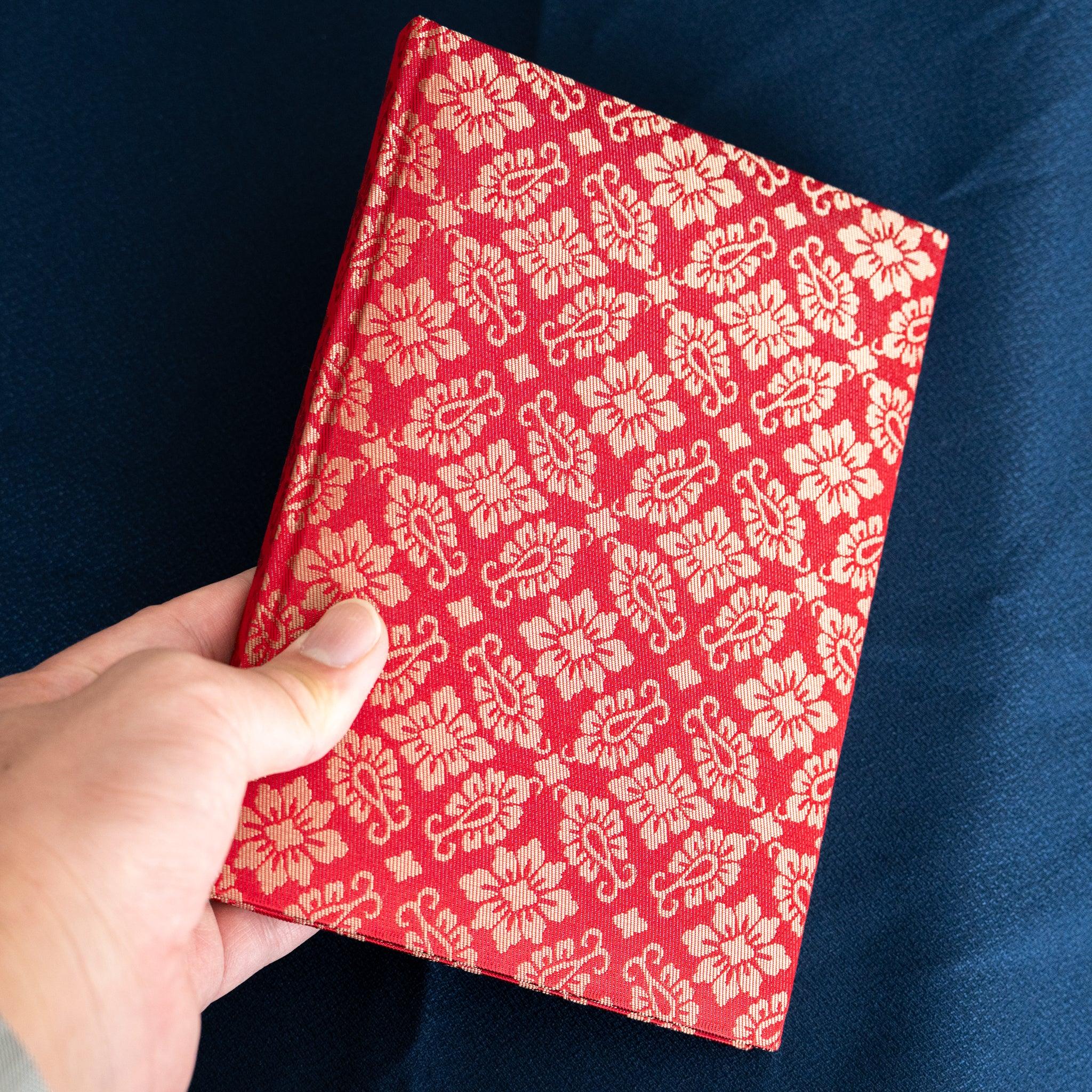 Hand holding Ko Aoi Nishijin silk Homeicho notebook showing full vermilion Ko Aoi floral cover, no paper band