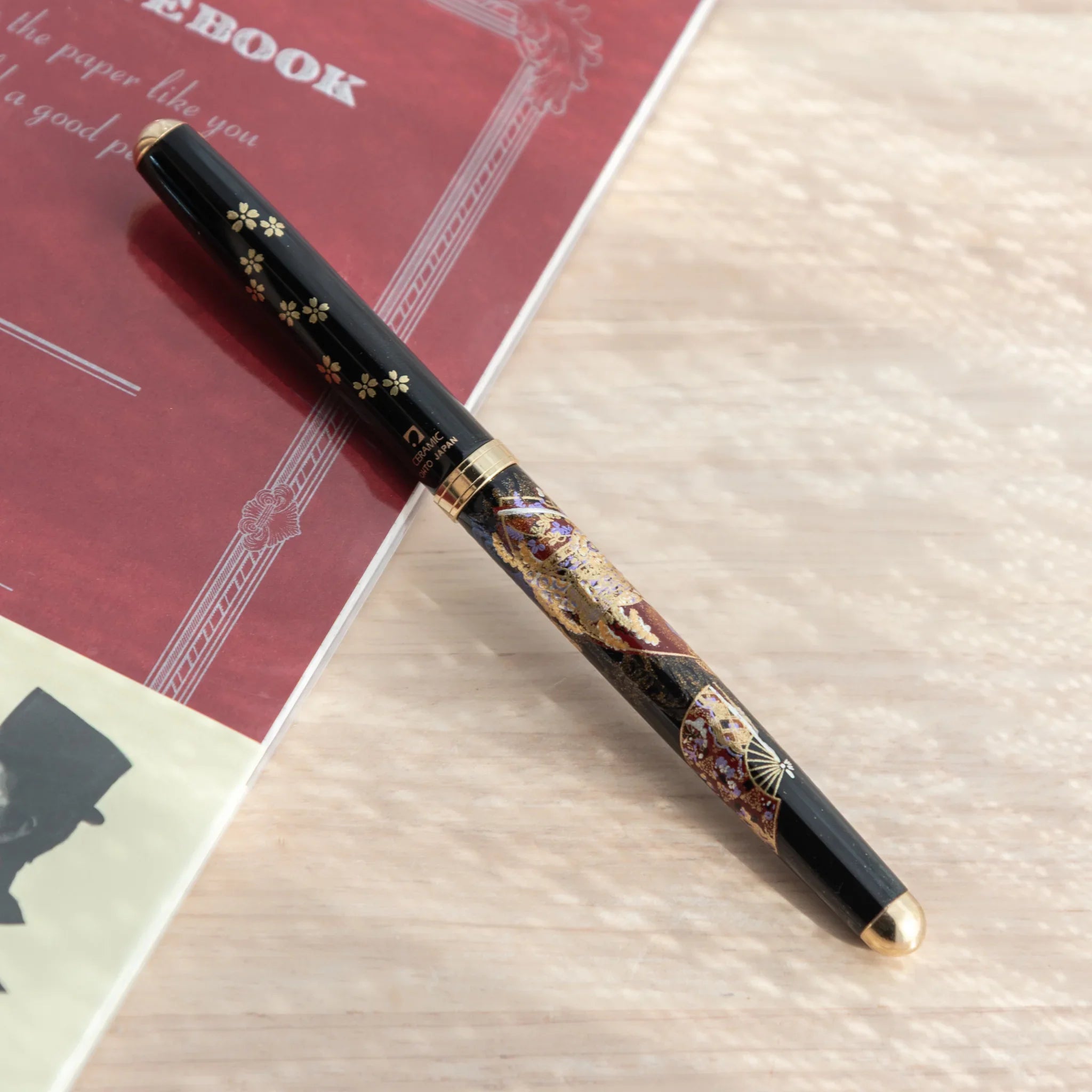 Black Yamanaka lacquer Japanese ballpoint pen with gold sakura cap decoration, angled view showing barrel Kyoto maki-e motifs