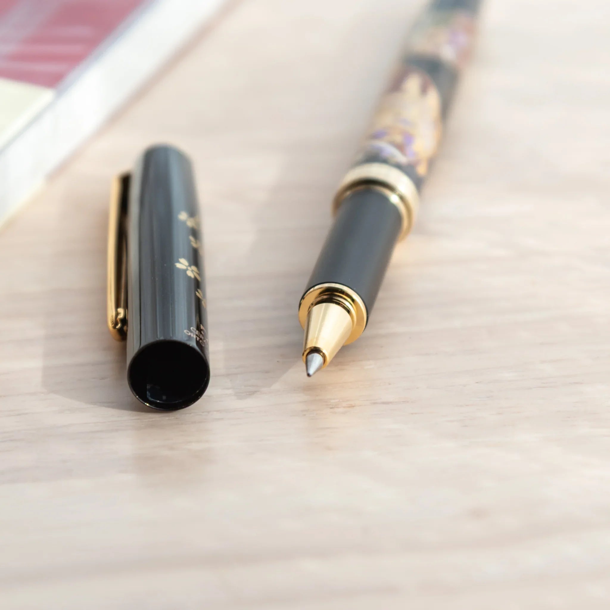 Kyoto Elegance Yamanaka Japanese ballpoint pen uncapped on wood surface showing gold tip and black barrel with floral pattern