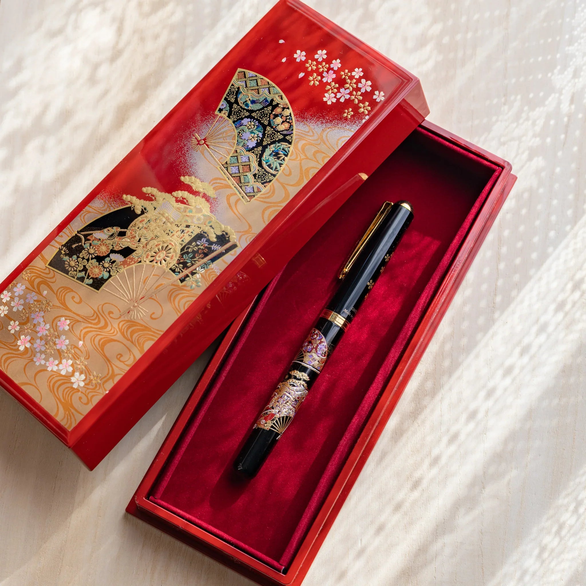 Japanese pen case open with fountain pen inside, lid adorned with gold fan and cherry blossom motifs