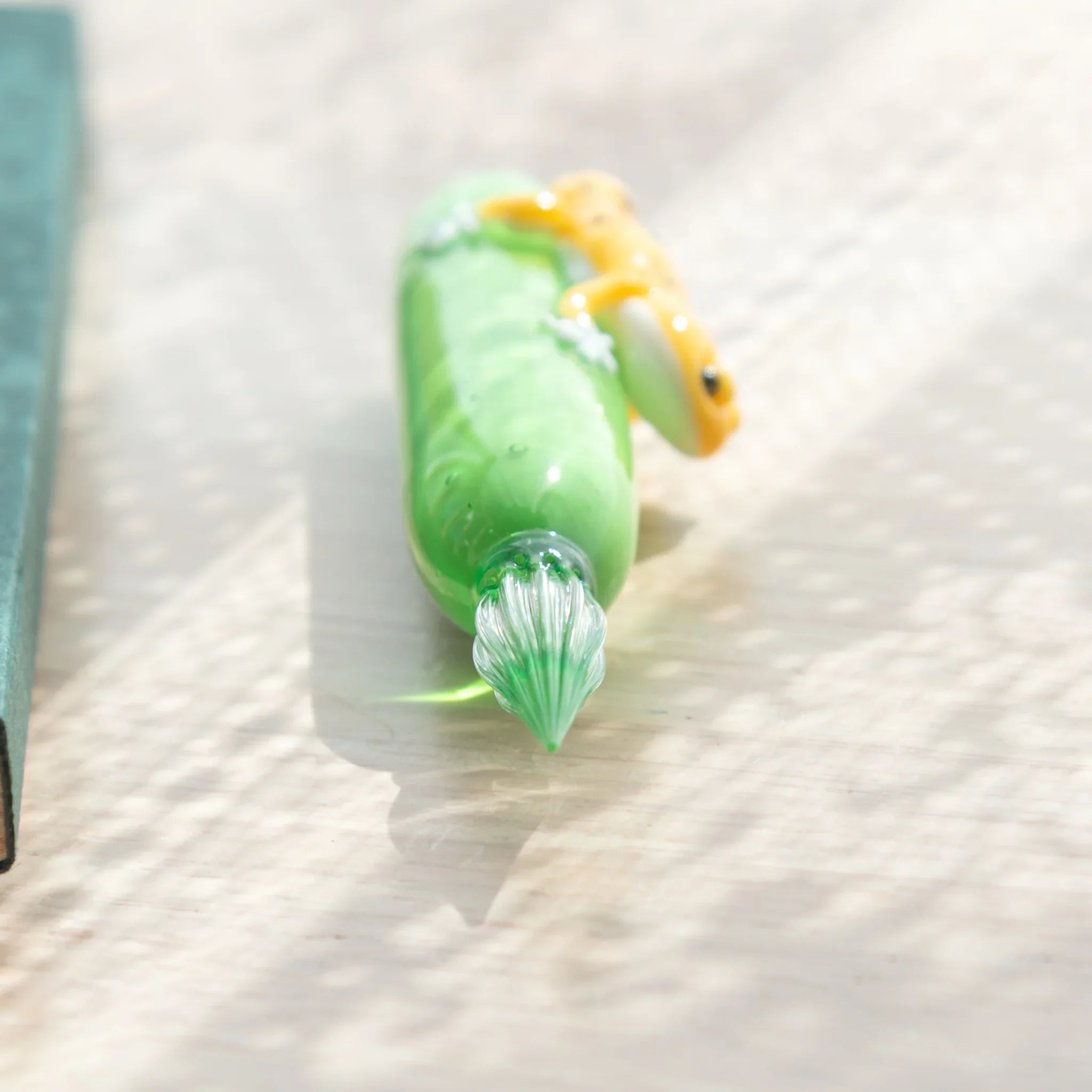 Close-up of ribbed glass nib on green glass dip pen, with yellow spotted leopard gecko figure partially visible at top