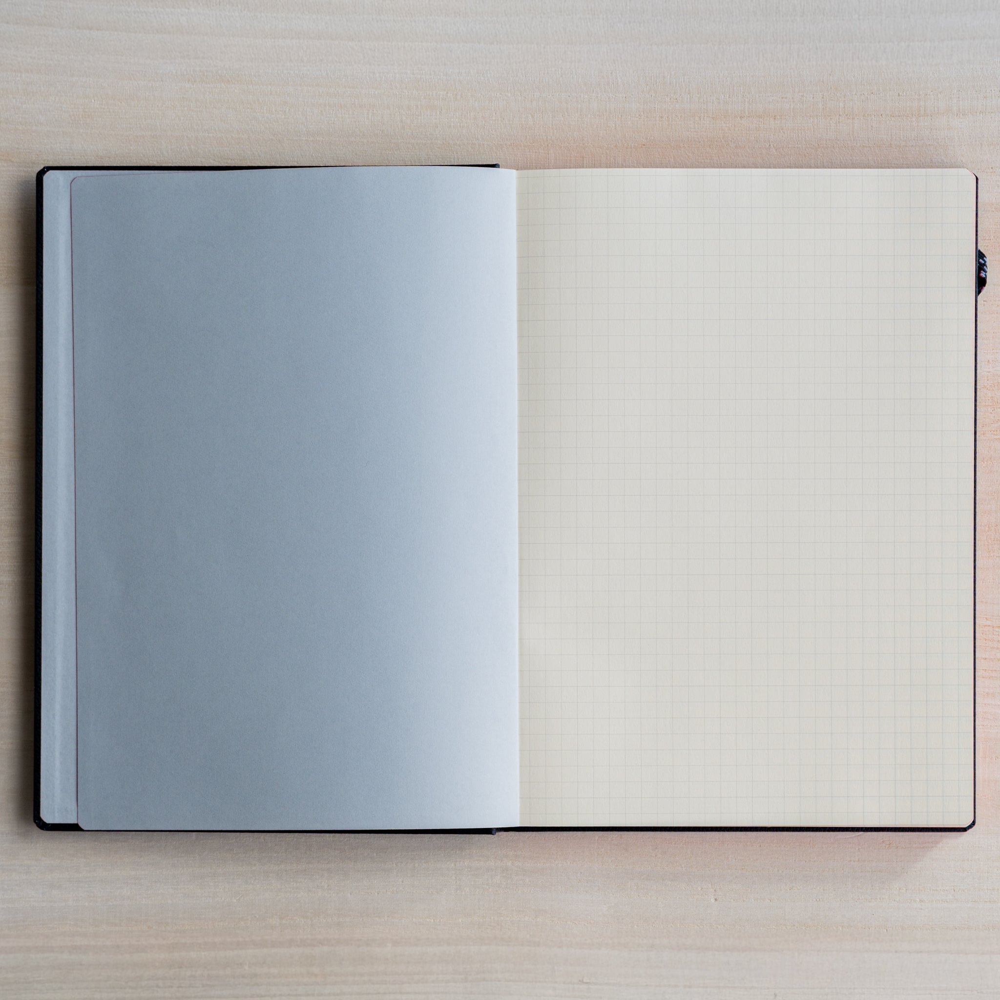 Life noble hard cover notebook A5 open flat showing gray flyleaf and cream grid L Writing Paper page on light desk