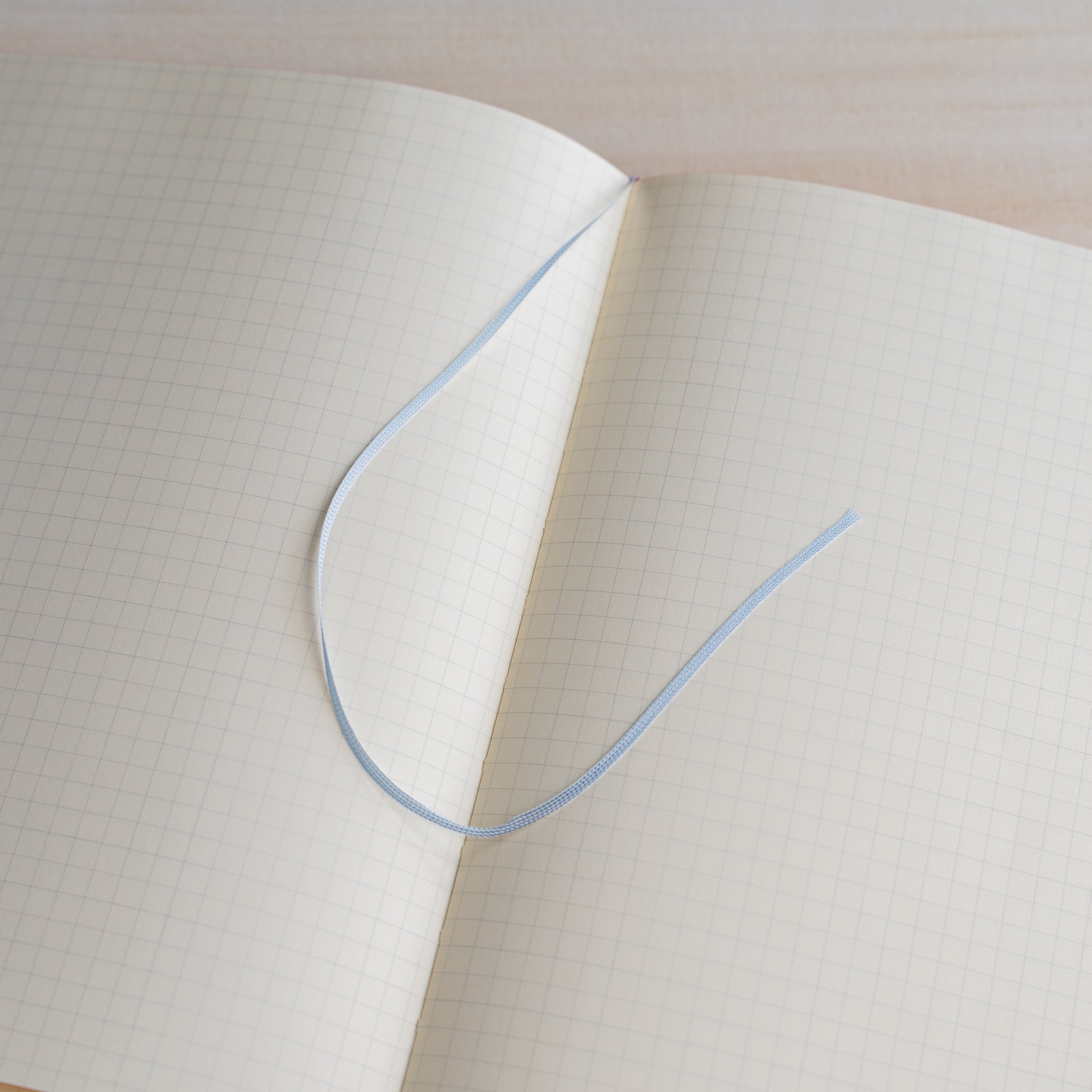 Life noble hard cover notebook A5 open flat showing cream grid L Writing Paper on both pages with blue ribbon bookmark