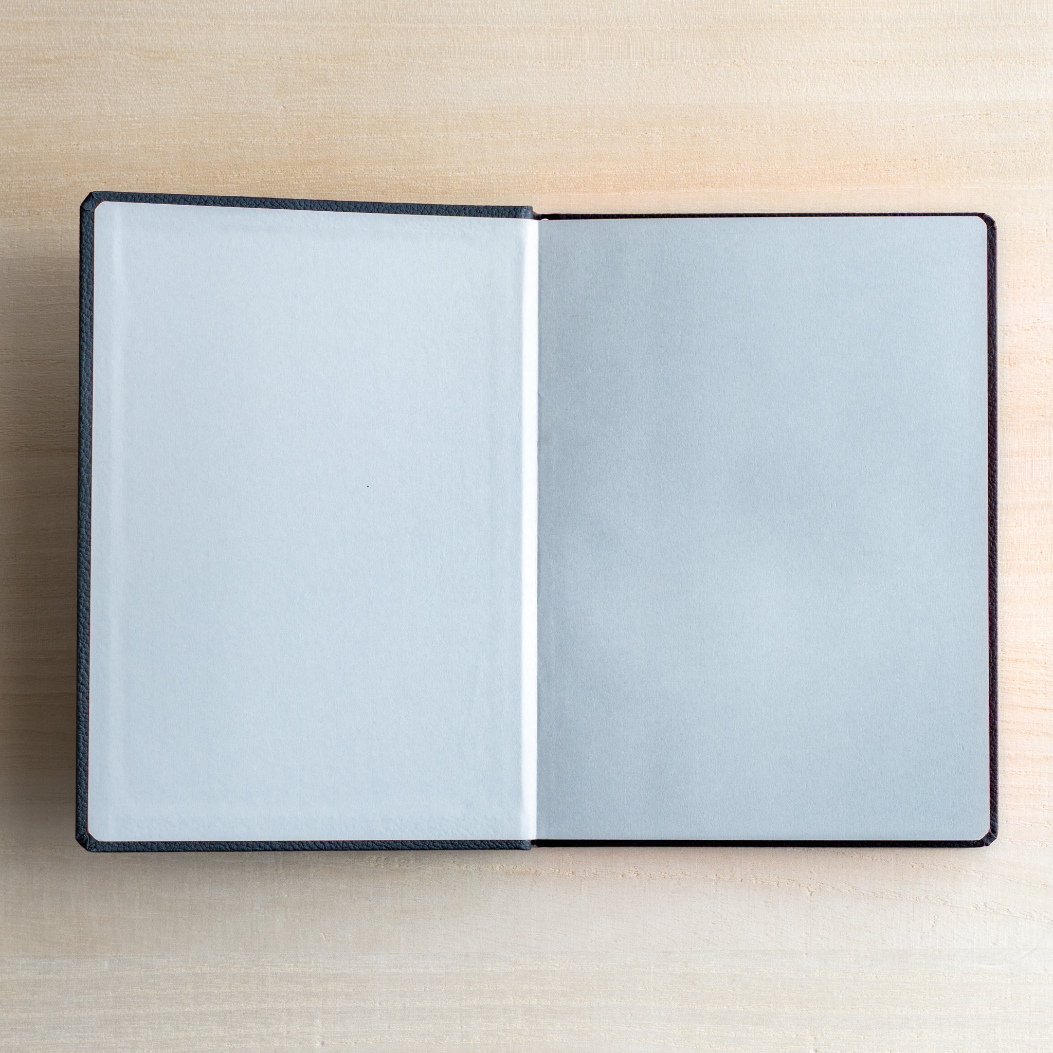 Life Noble notebook A6 open flat on desk, showing pale gray flyleaf and cream L Writing Paper with clean