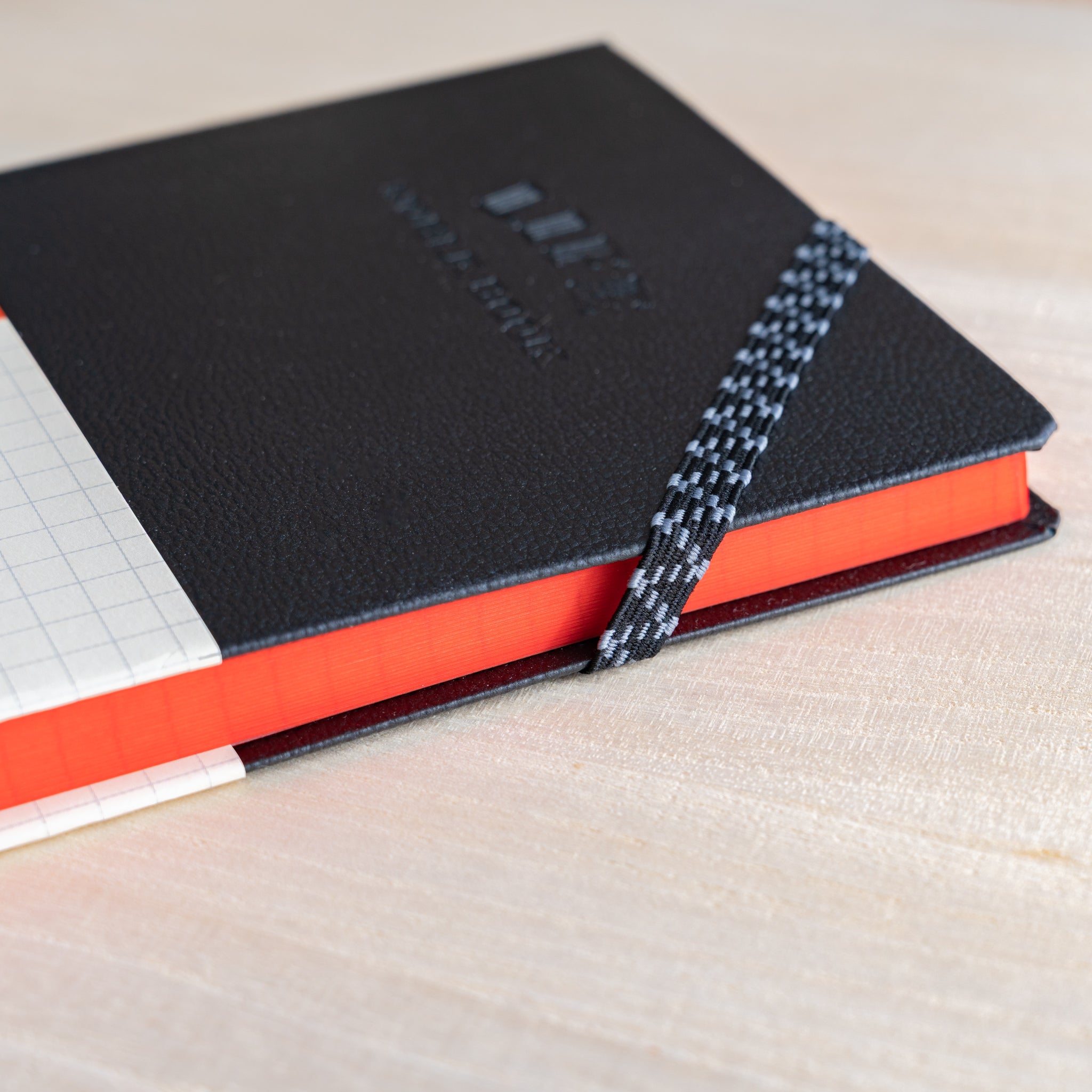 Life Noble notebook A6 hard cover with elastic band and red page edges on desk, showing compact Japanese notebook craftsmanship