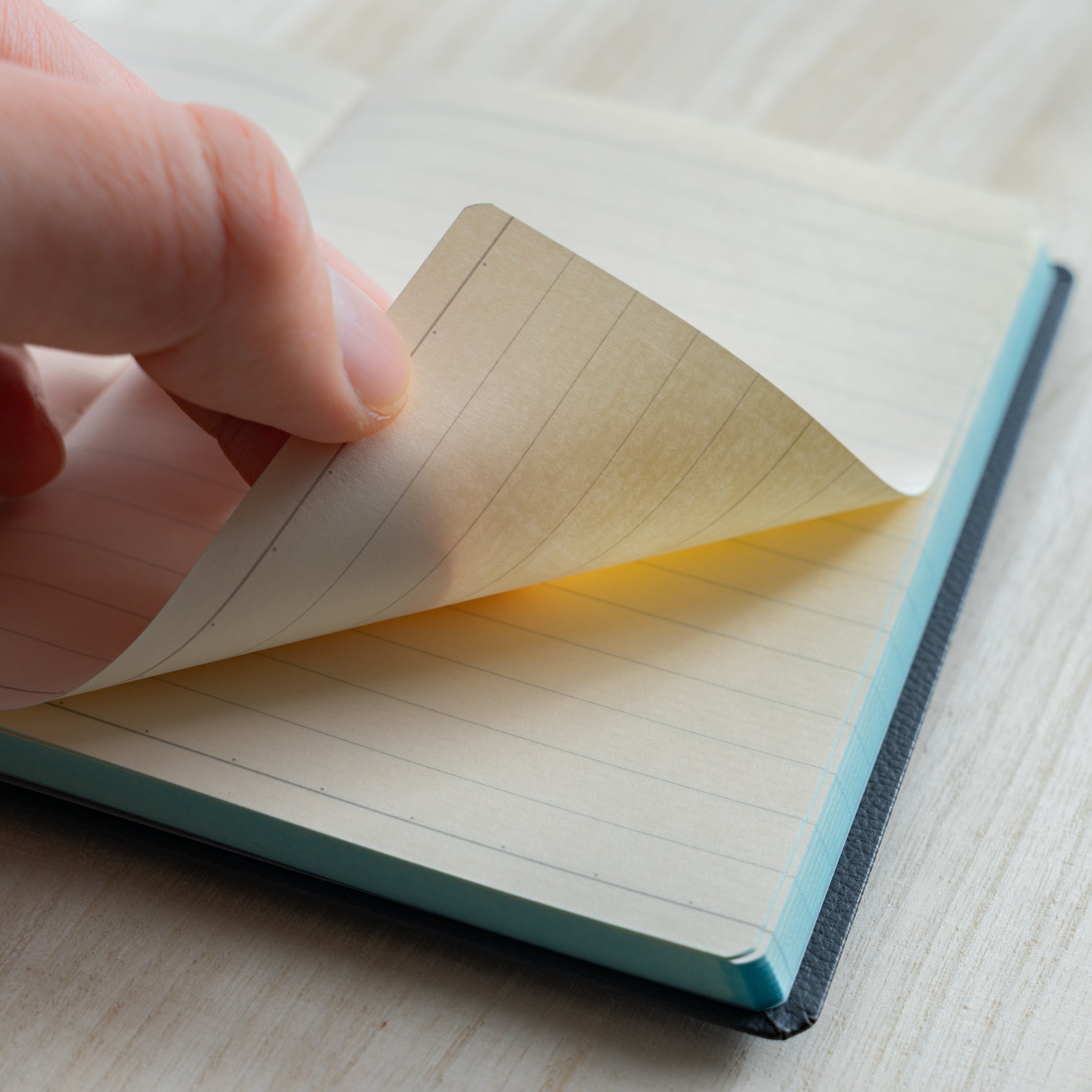 Life Noble notebook A6 close-up of hand turning lined L Writing Paper, showing cream pages and smooth texture
